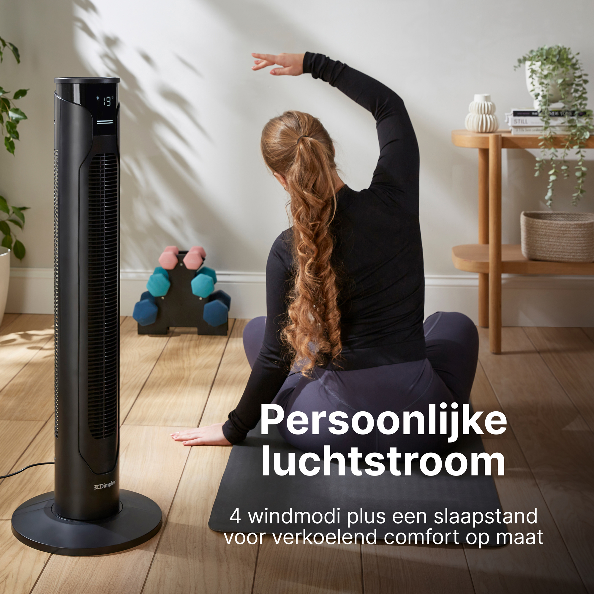 Zwarte torenventilator naast een vrouw die yoga doet op een mat.