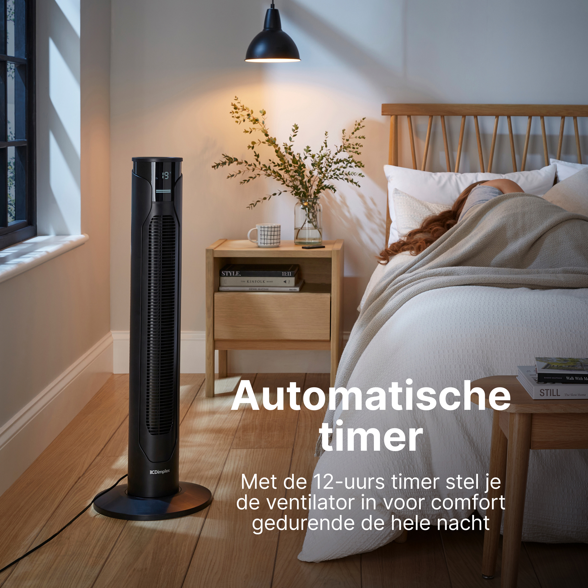 Een zwarte torenventilator staat naast een bed met slapend persoon.