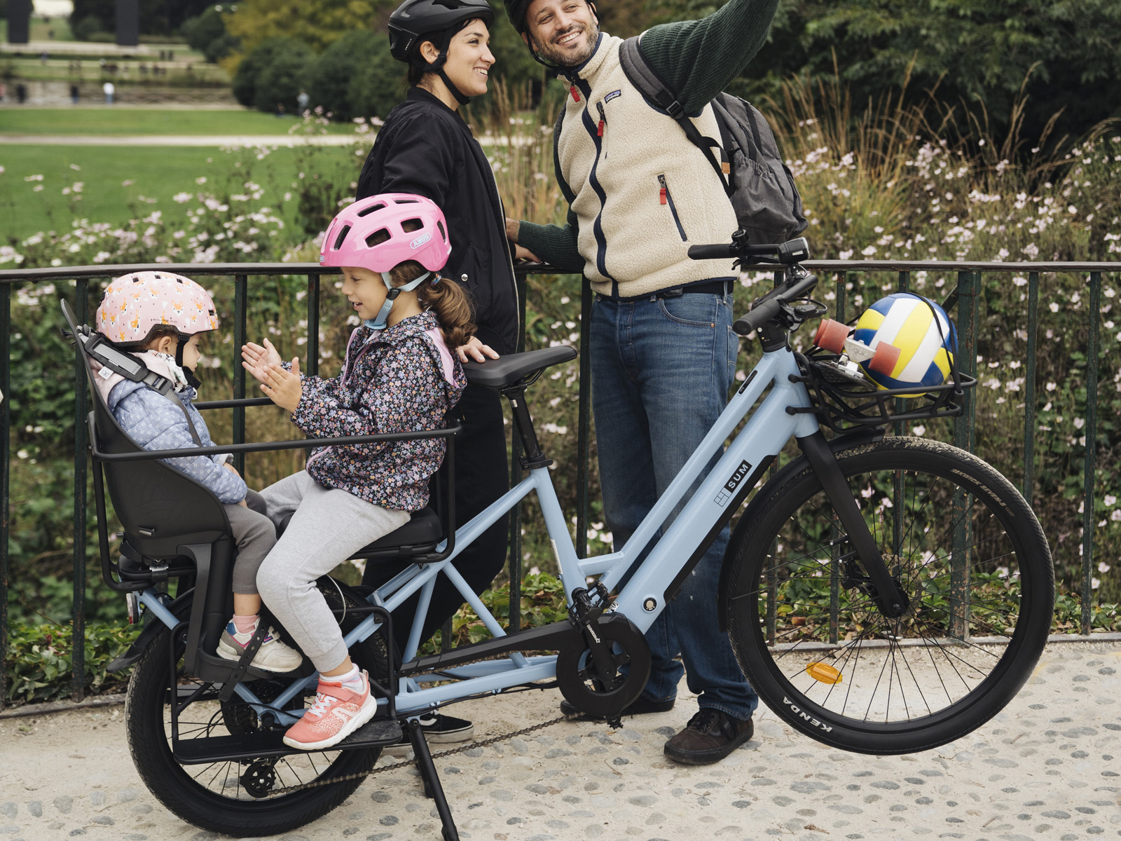 Familie mit Kindern auf einem Lastenfahrrad im Park, sie tragen Helme.