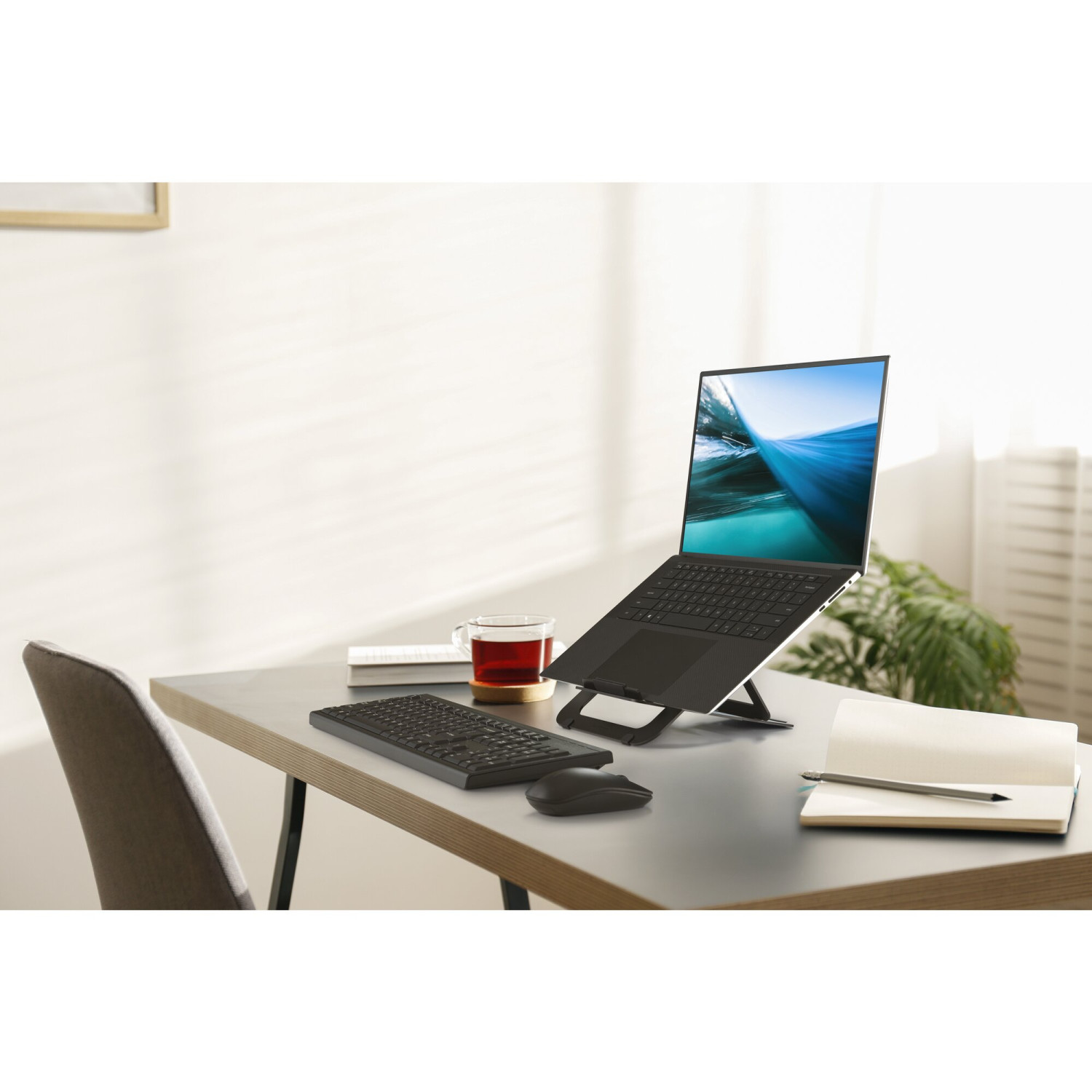 Un ordinateur portable, un clavier, une souris et du thé sur un bureau. Une chaise est à proximité.