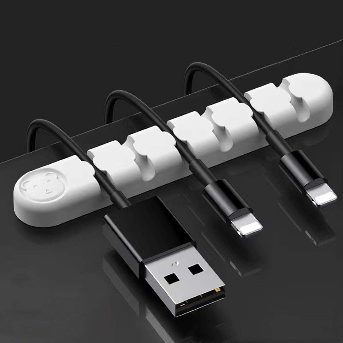 Biały organizer na kable z misiem trzyma czarne kable. Z przodu złącze USB.