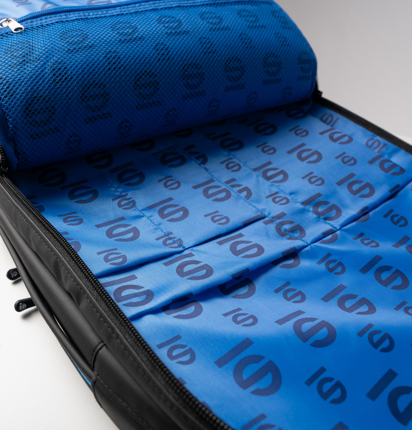 Ein geöffneter schwarzer Rucksack mit blauem Innenfutter mit wiederholtem Logo.