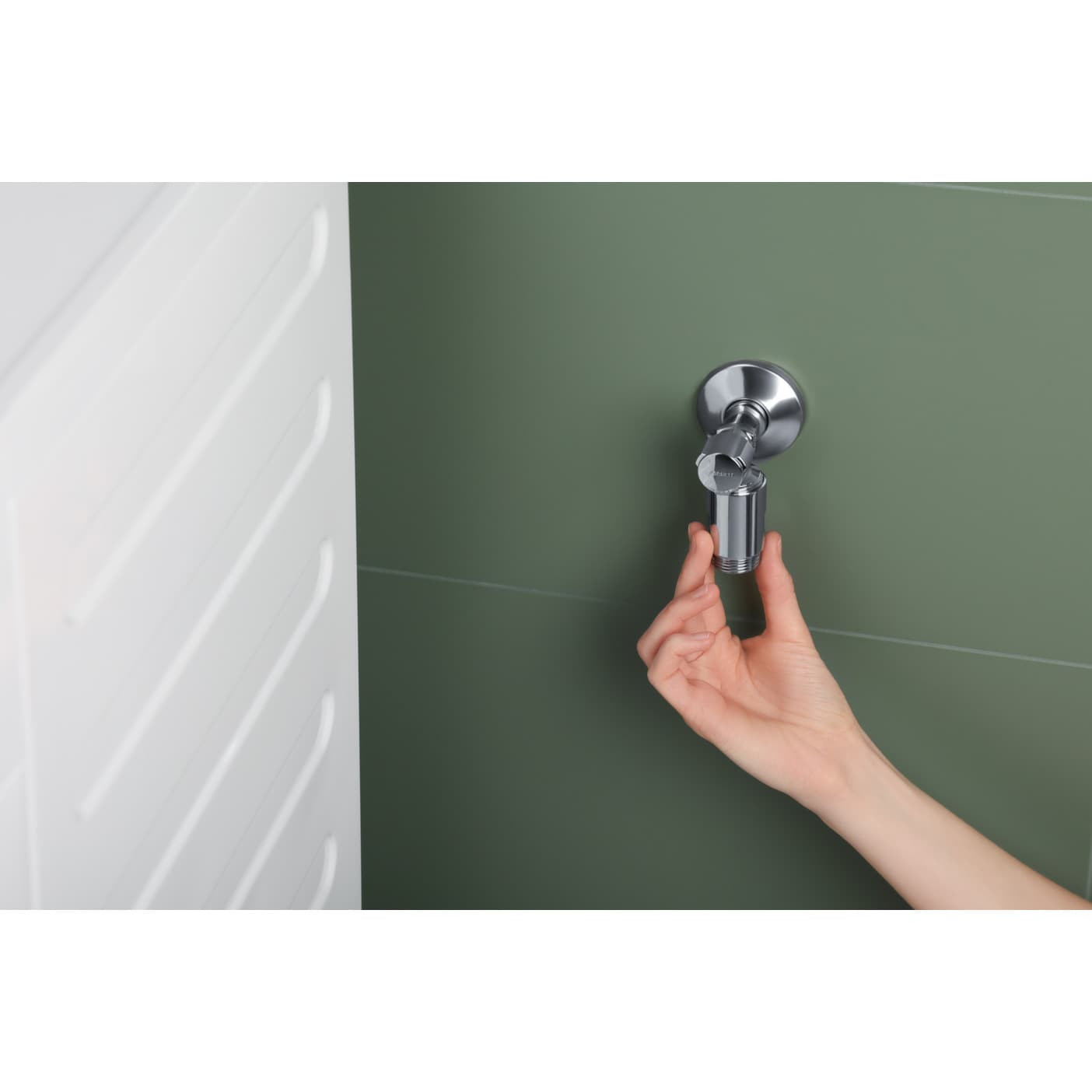 Mano tiene accessorio rubinetto argento contro muro verde.