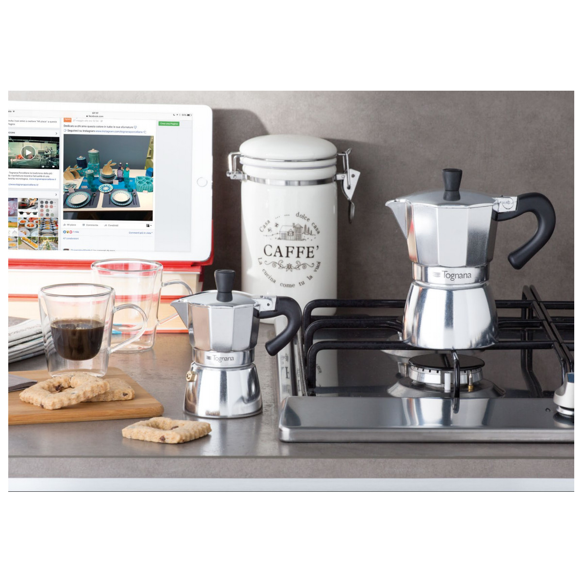 Due moka, un bicchiere di caffè, biscotti e un barattolo su un fornello.
