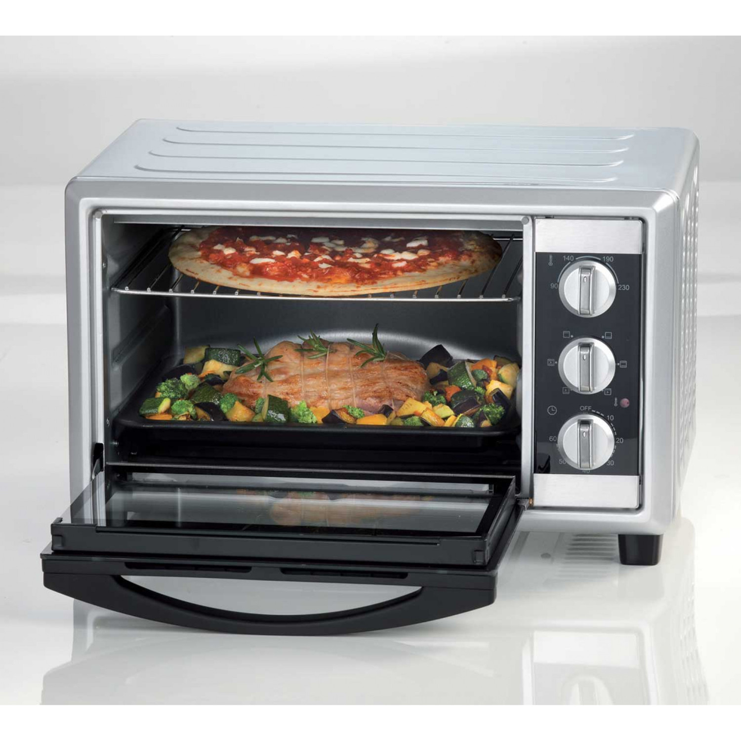 Un horno tostador plateado con pizza en la rejilla superior y carne con verduras en la inferior.