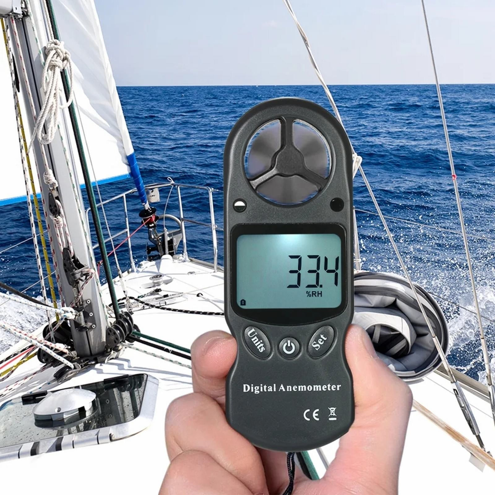 Ein Mann hält ein schwarzes Digital-Anemometer auf dem Deck eines Segelboots im Meer.