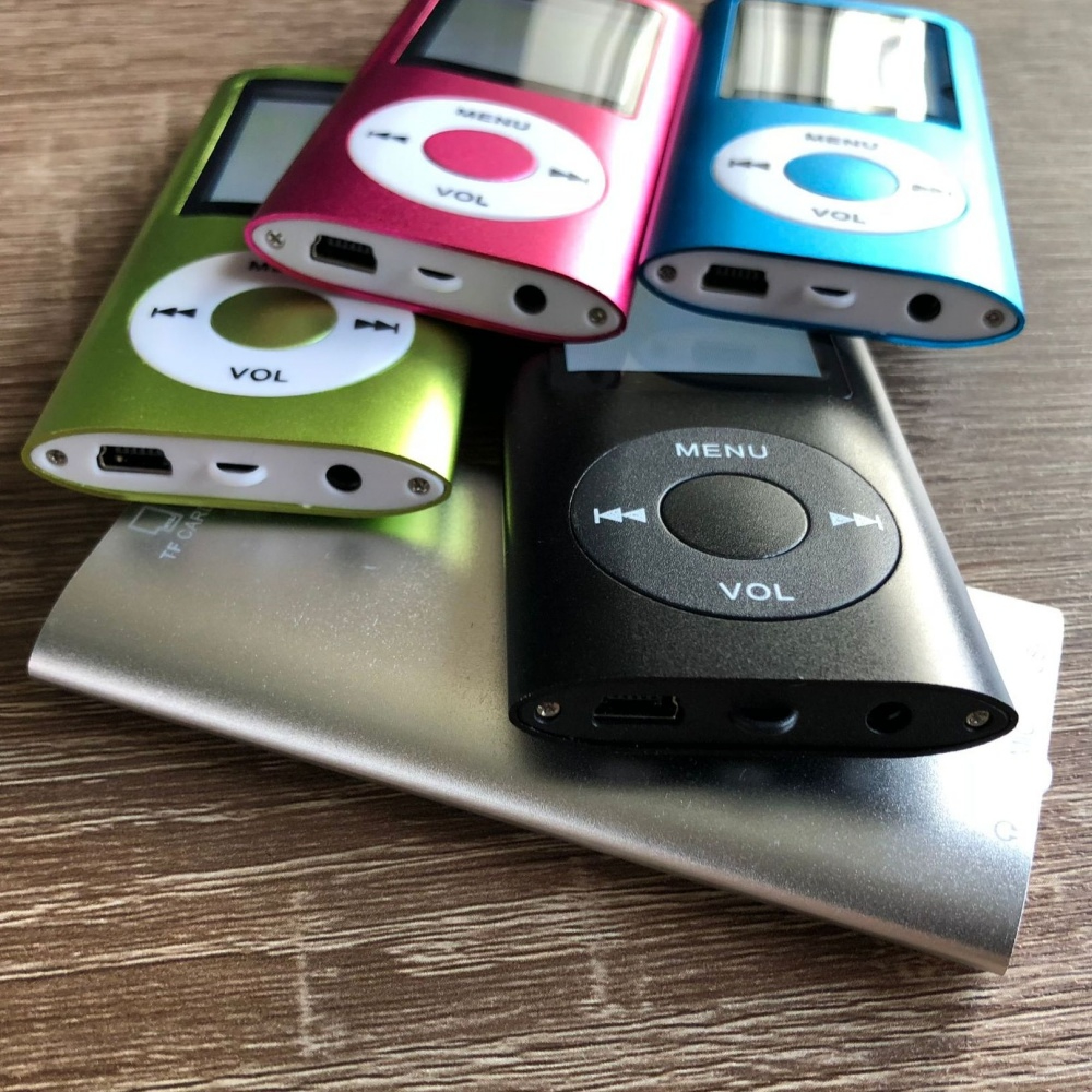 Vier MP3-Player in Grün, Pink, Blau und Schwarz liegen auf silbernen Powerbanks.