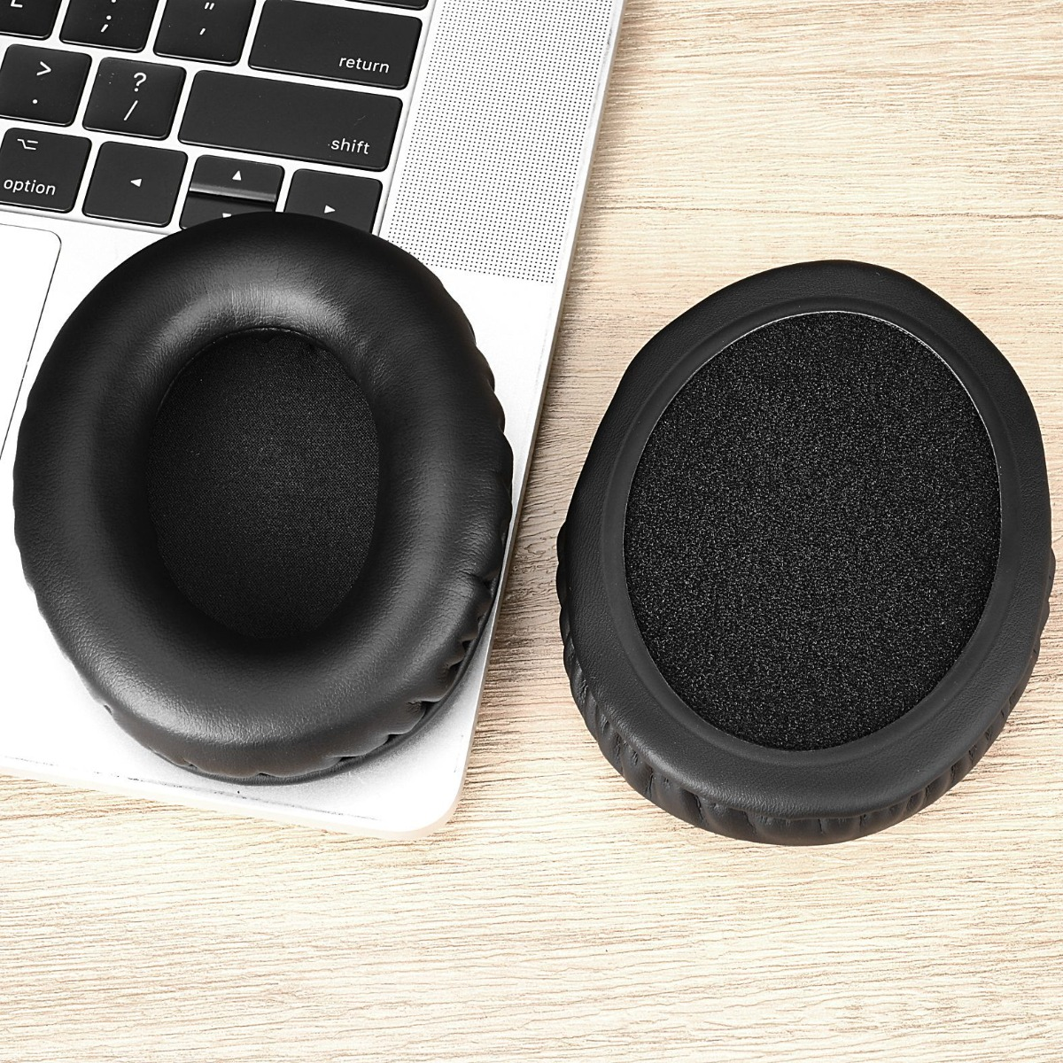 Zwei schwarze Ohrpolster liegen auf einer Tastatur und einer Holzoberfläche.