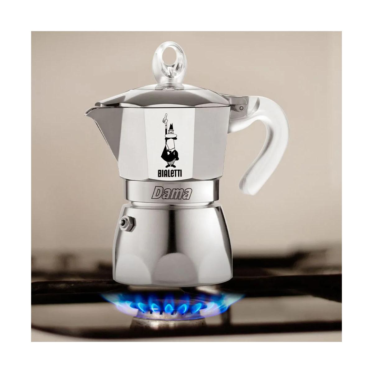 Una cafetera Moka Bialetti con el logo del hombrecito sobre un hornillo de gas con llama azul.