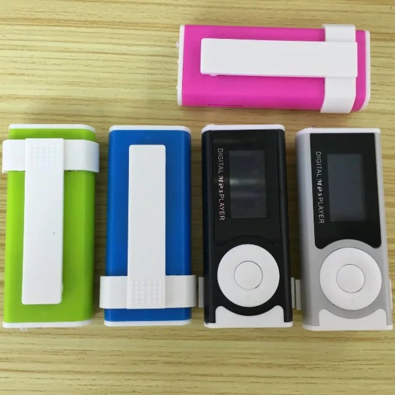 Vier MP3-Player in Grün, Blau, Schwarz und Silber mit weißen Clips und einem rosafarbenen Player oben.