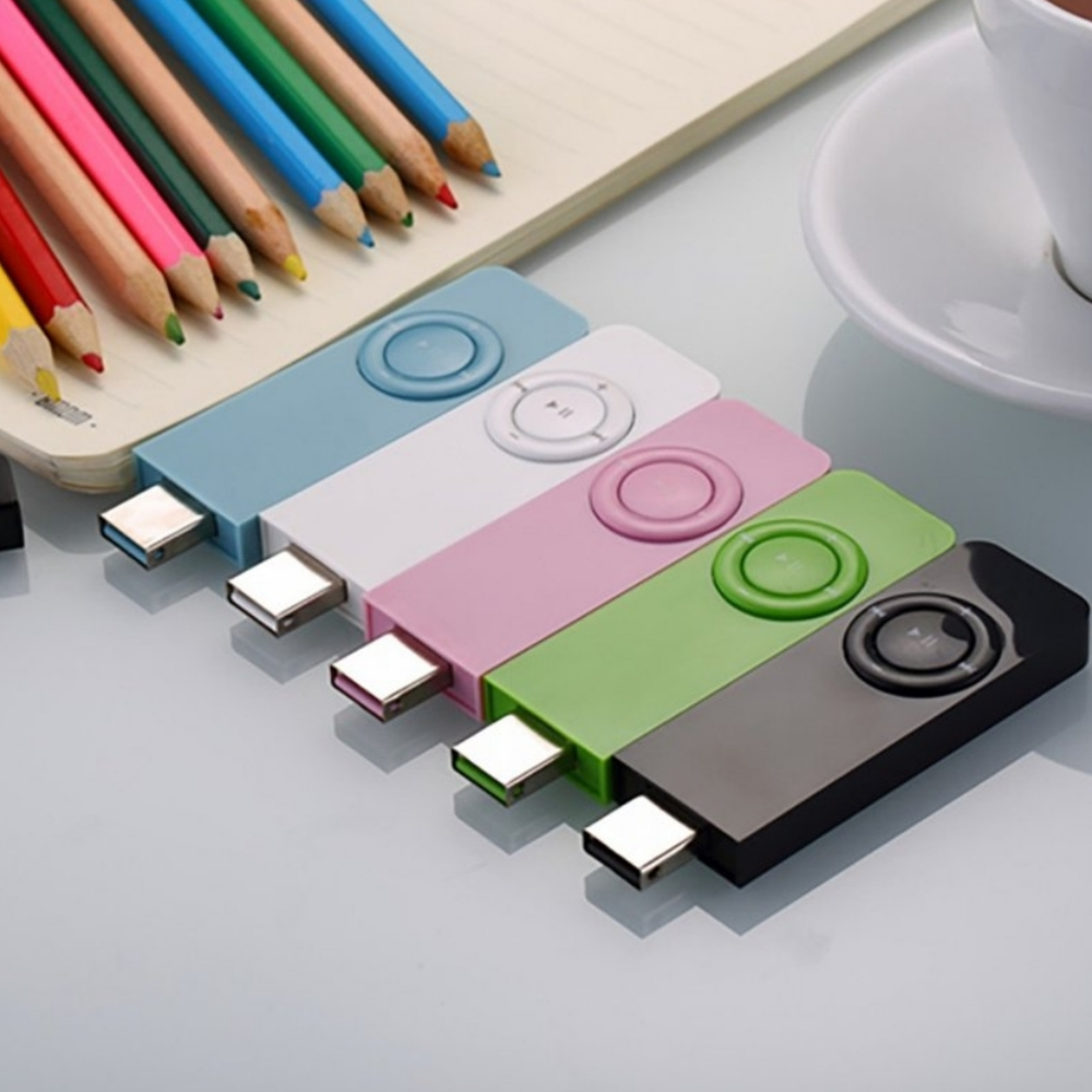 Bunte Stifte liegen neben einem Notizbuch und mehreren USB-Sticks in Pastellfarben.