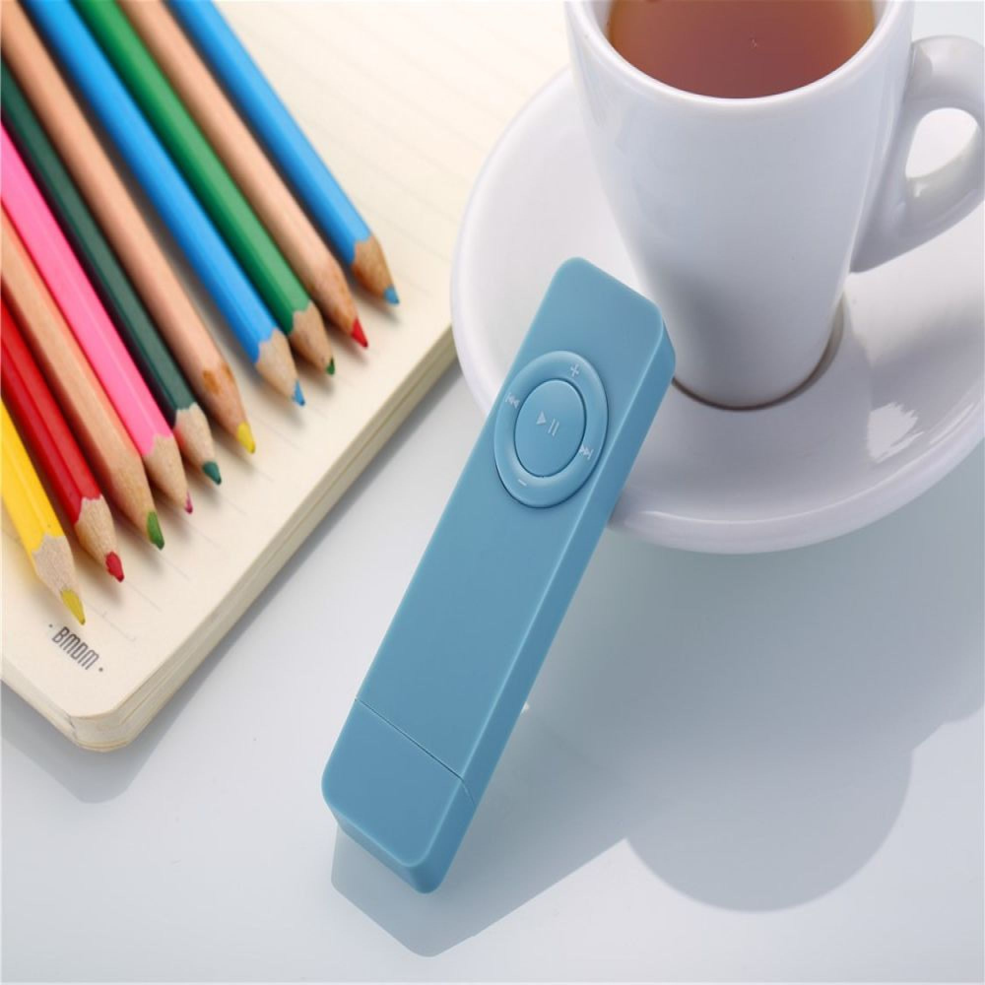 Blauer MP3-Player mit Tasten, daneben Buntstifte auf einem Notizbuch und eine Tasse Tee.