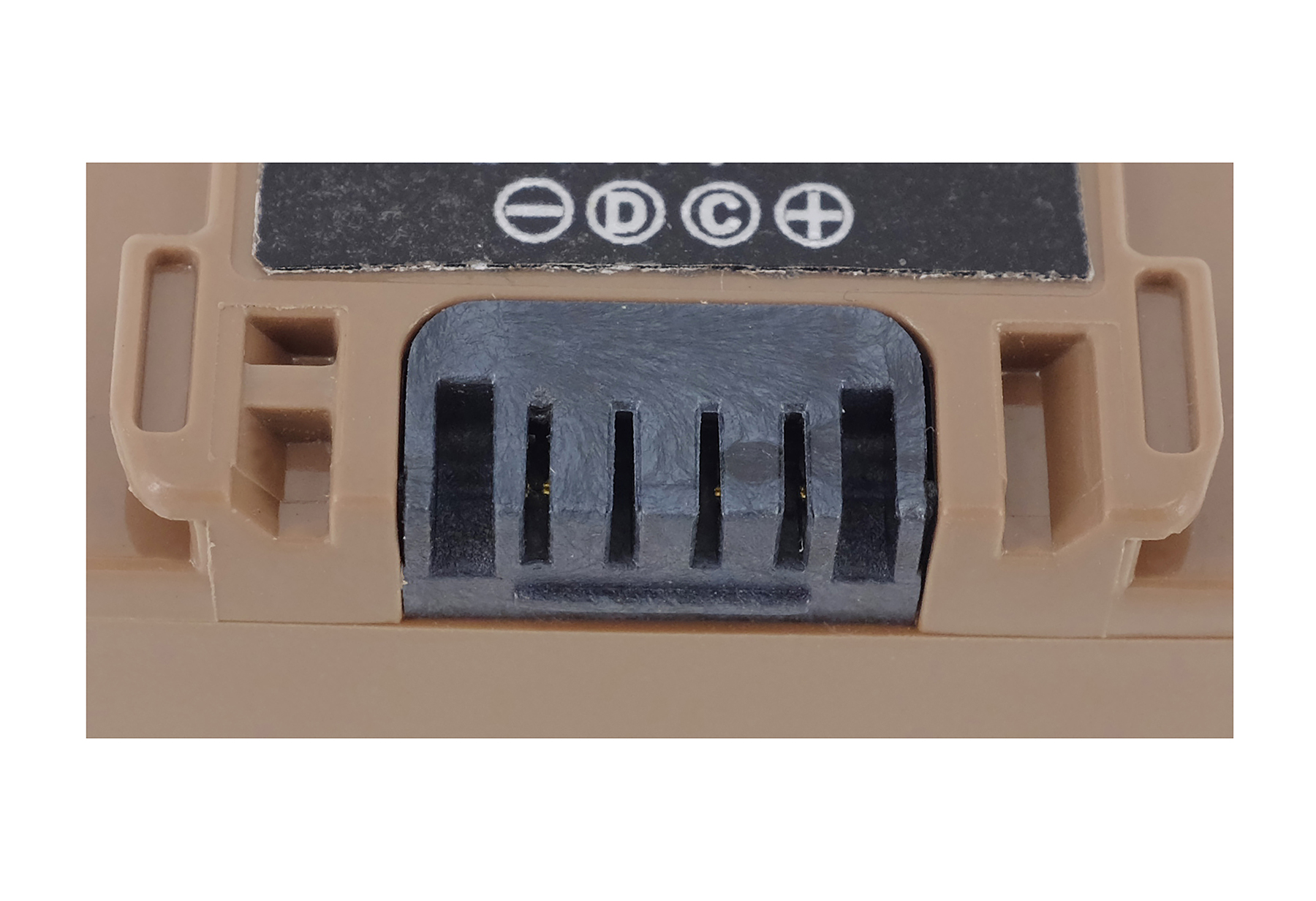 Nahaufnahme eines braunen Batterieanschlusses mit schwarzen Kontakten und Symbolen.