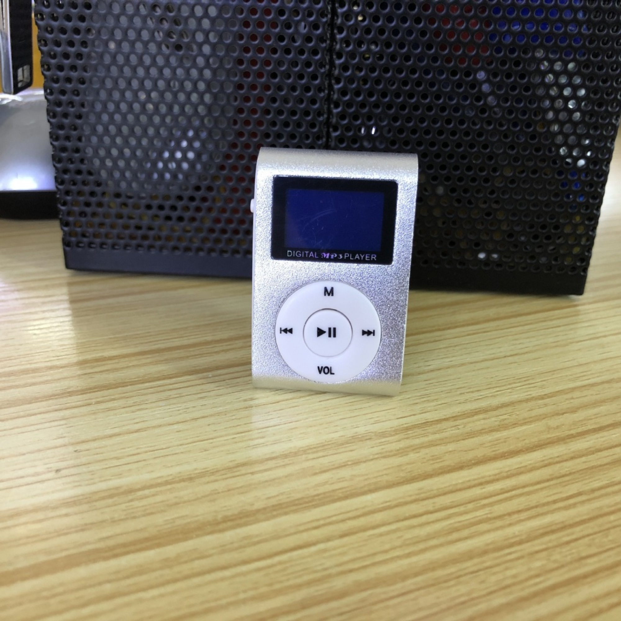 Kleiner silberner MP3-Player mit blauen Bildschirm und Bedienelementen auf Holztisch.