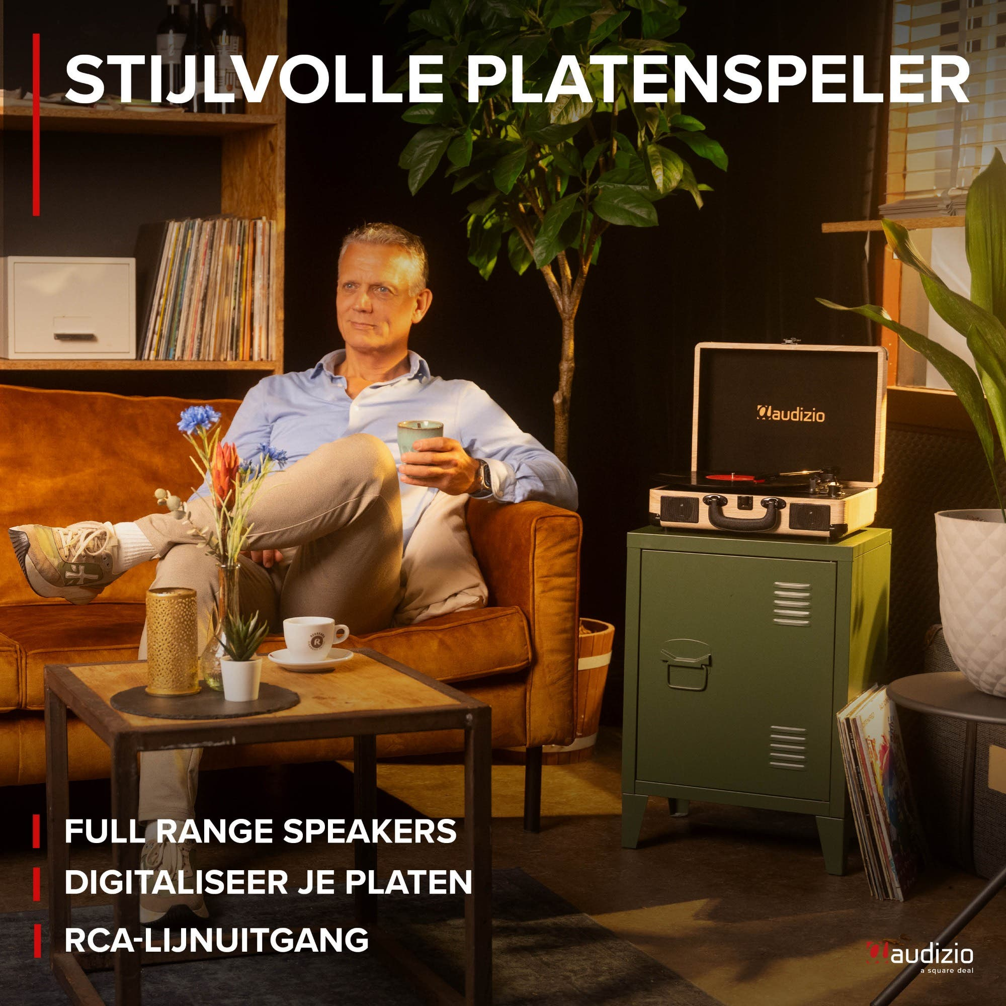 Man sits on sofa, holding cup, turntable on cabinet.