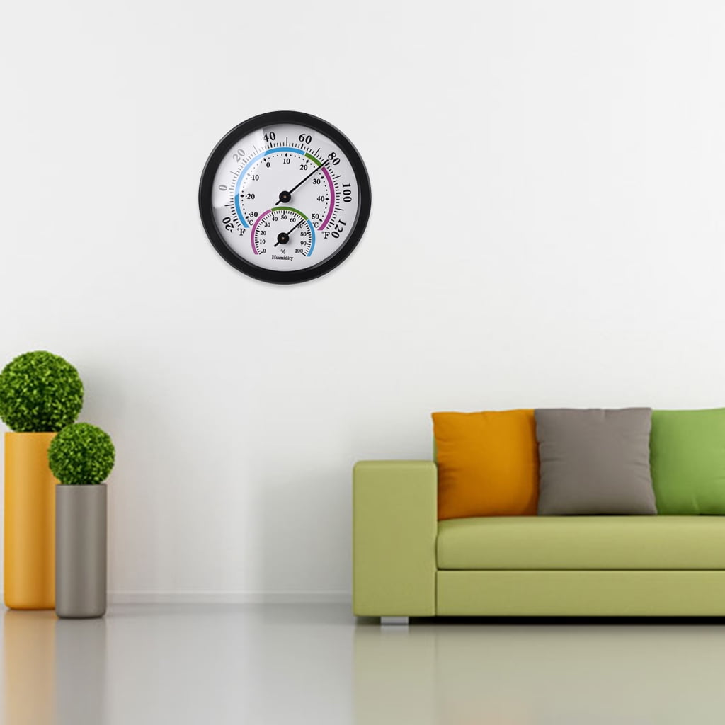 Ein runder Thermometer/Hygrometer an einer weißen Wand über einer grünen Couch mit bunten Kissen.