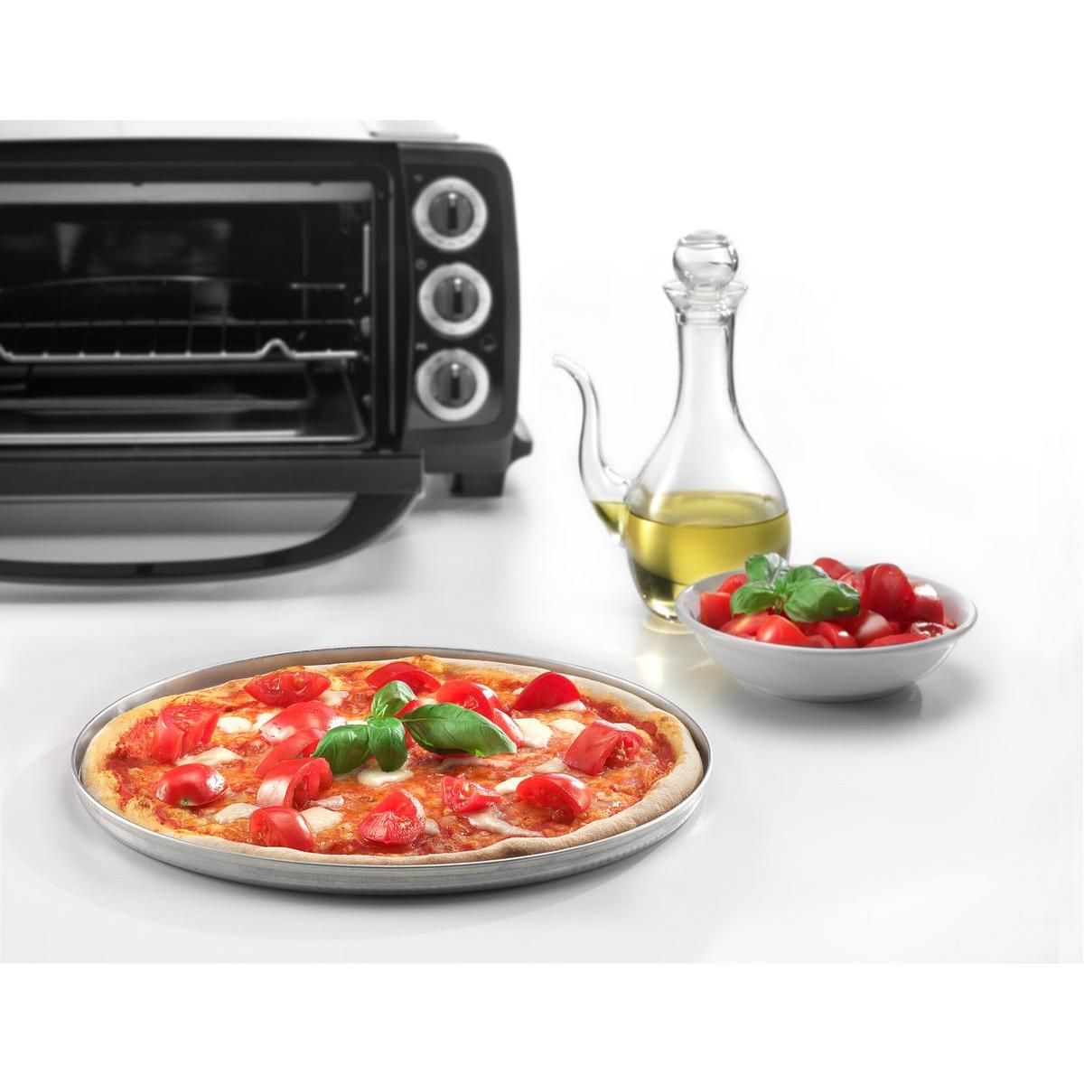 Una pizza Margarita con tomate, mozzarella y albahaca junto a un vaso de aceite de oliva y un cuenco de tomates cherry.