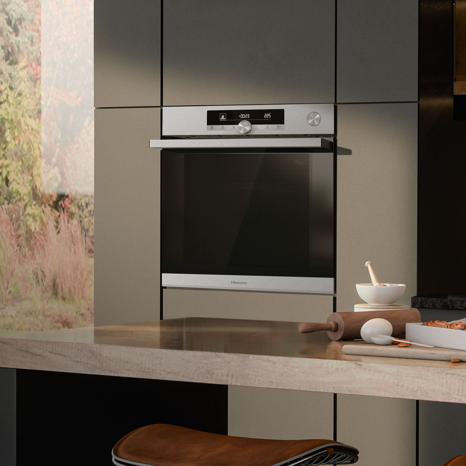 Un moderno forno Hisense in una cucina, con vista su un giardino lussureggiante. Utensili da forno sul bancone.