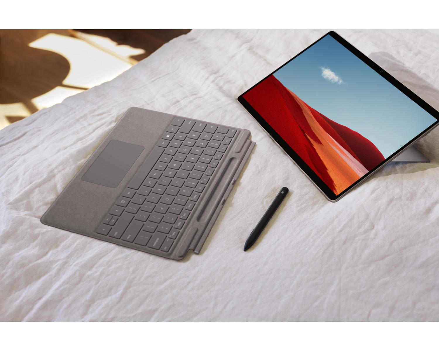 Een grijze tablet met toetsenbord en pen liggen op een wit bed.