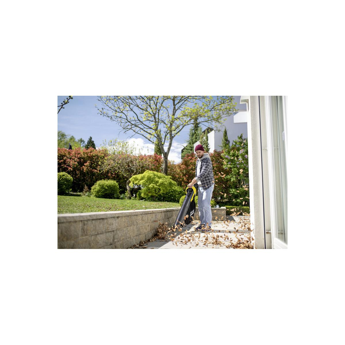 Mann bläst Blätter mit einem Laubbläser auf einem gepflasterten Weg im Garten weg.