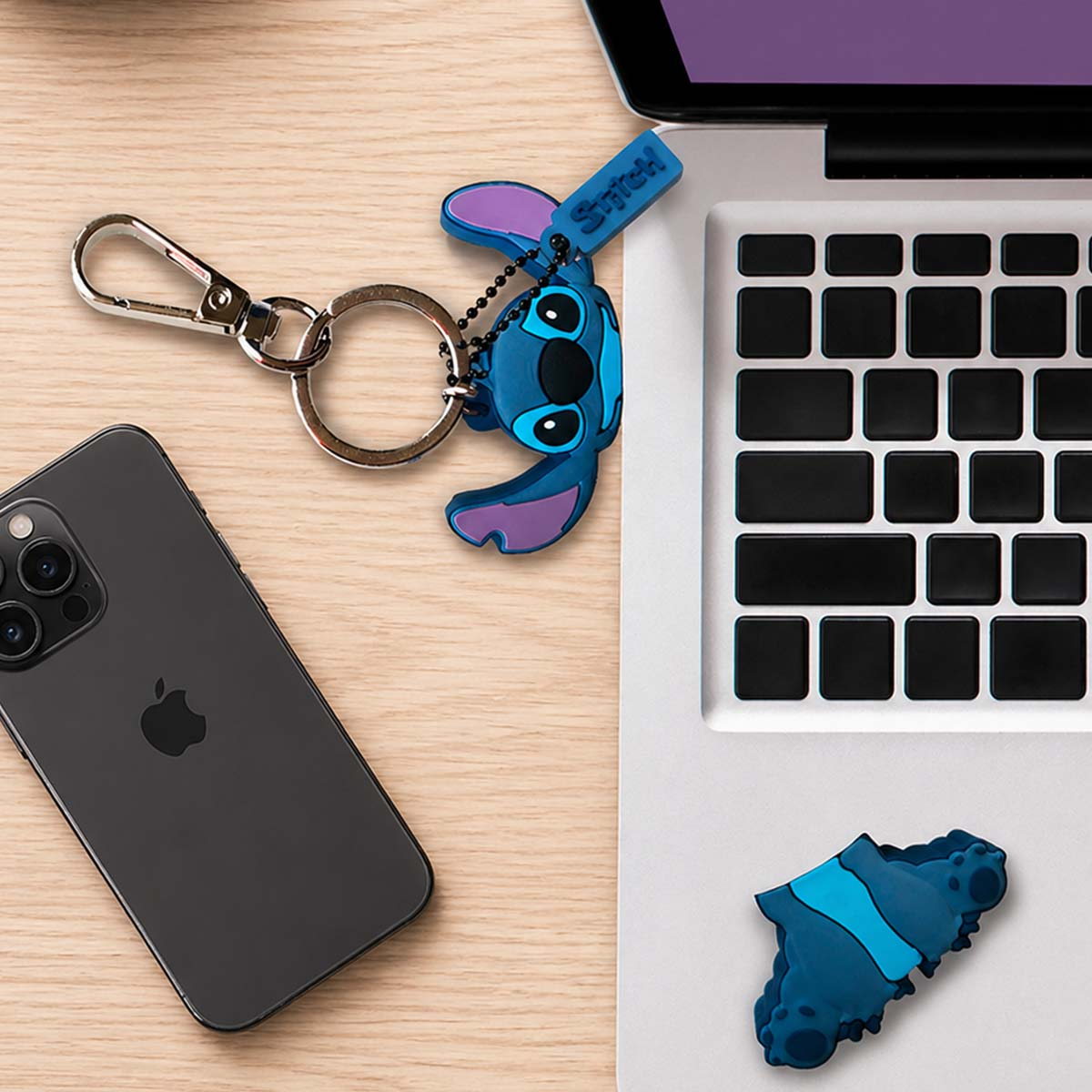 Un portachiavi blu di Stitch accanto a un iPhone nero e tastiera di laptop.