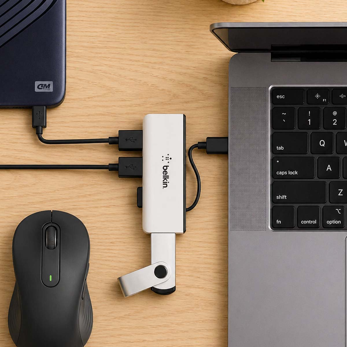 Un laptop, mouse, hard disk esterno e hub USB su una scrivania di legno.