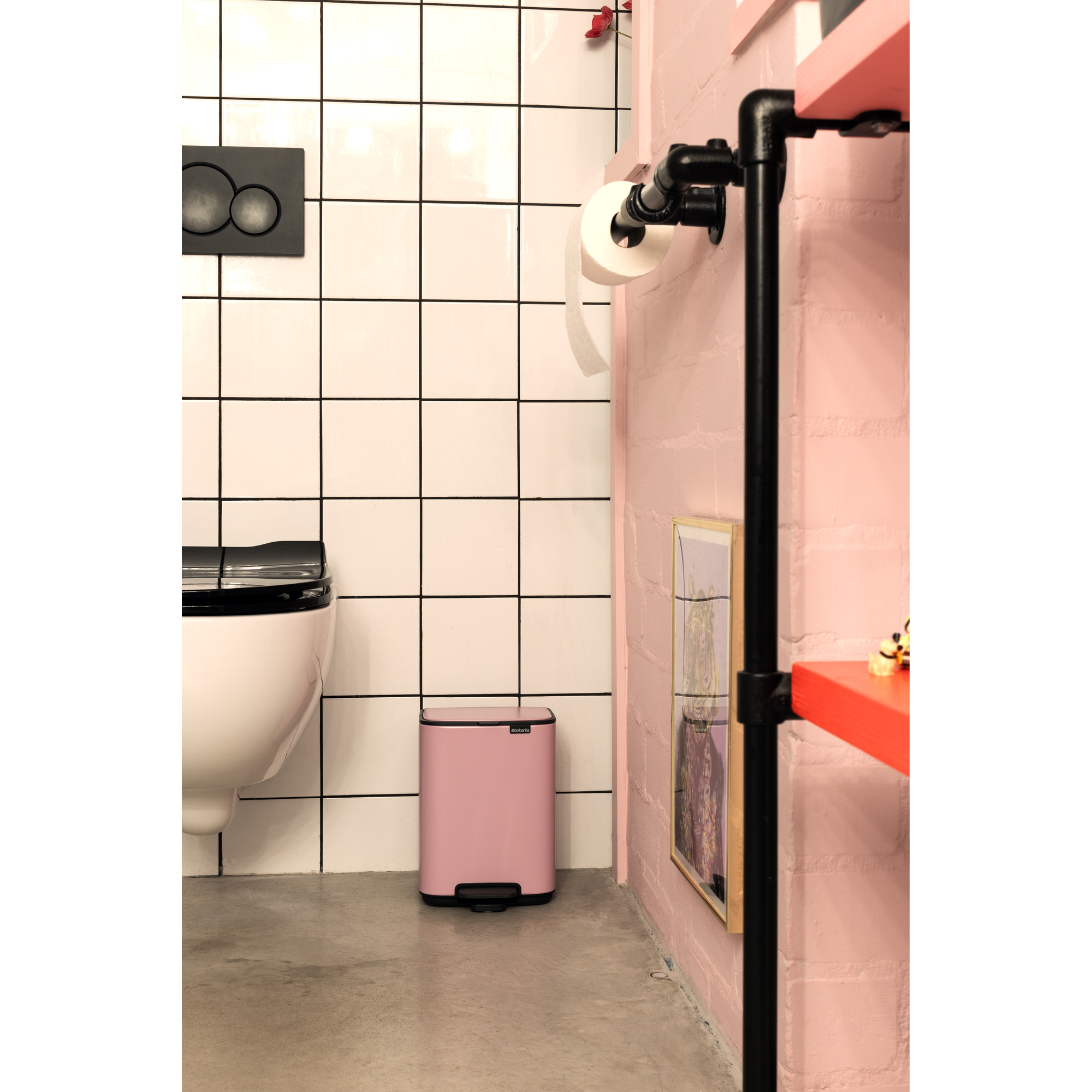 Een roze prullenbak staat naast een wit toilet met zwart deksel.