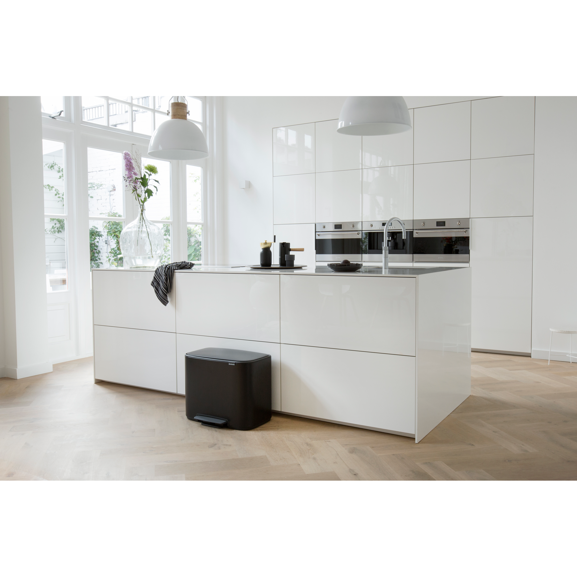 Moderne witte keuken met eiland, apparaten en een zwarte prullenbak.