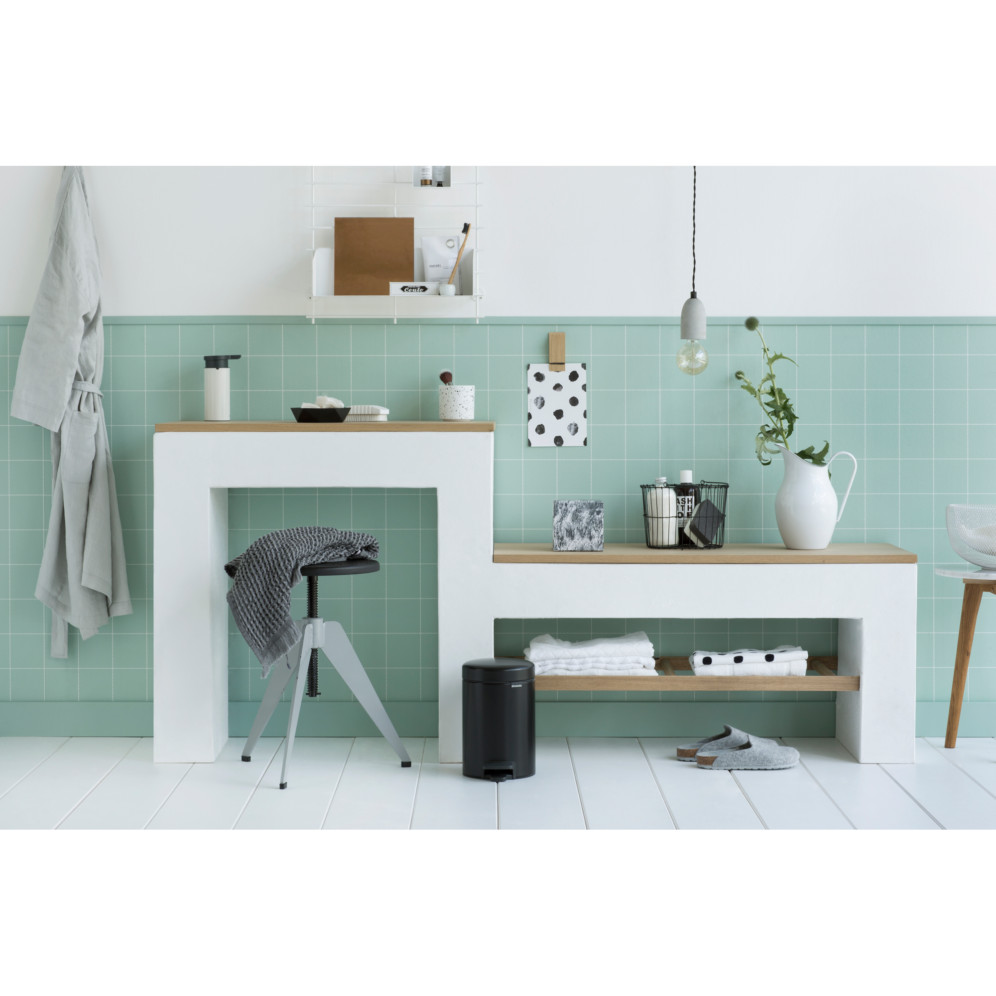 Badkamer met mintgroene tegels, wit meubilair, handdoeken, een kruk en een mand.