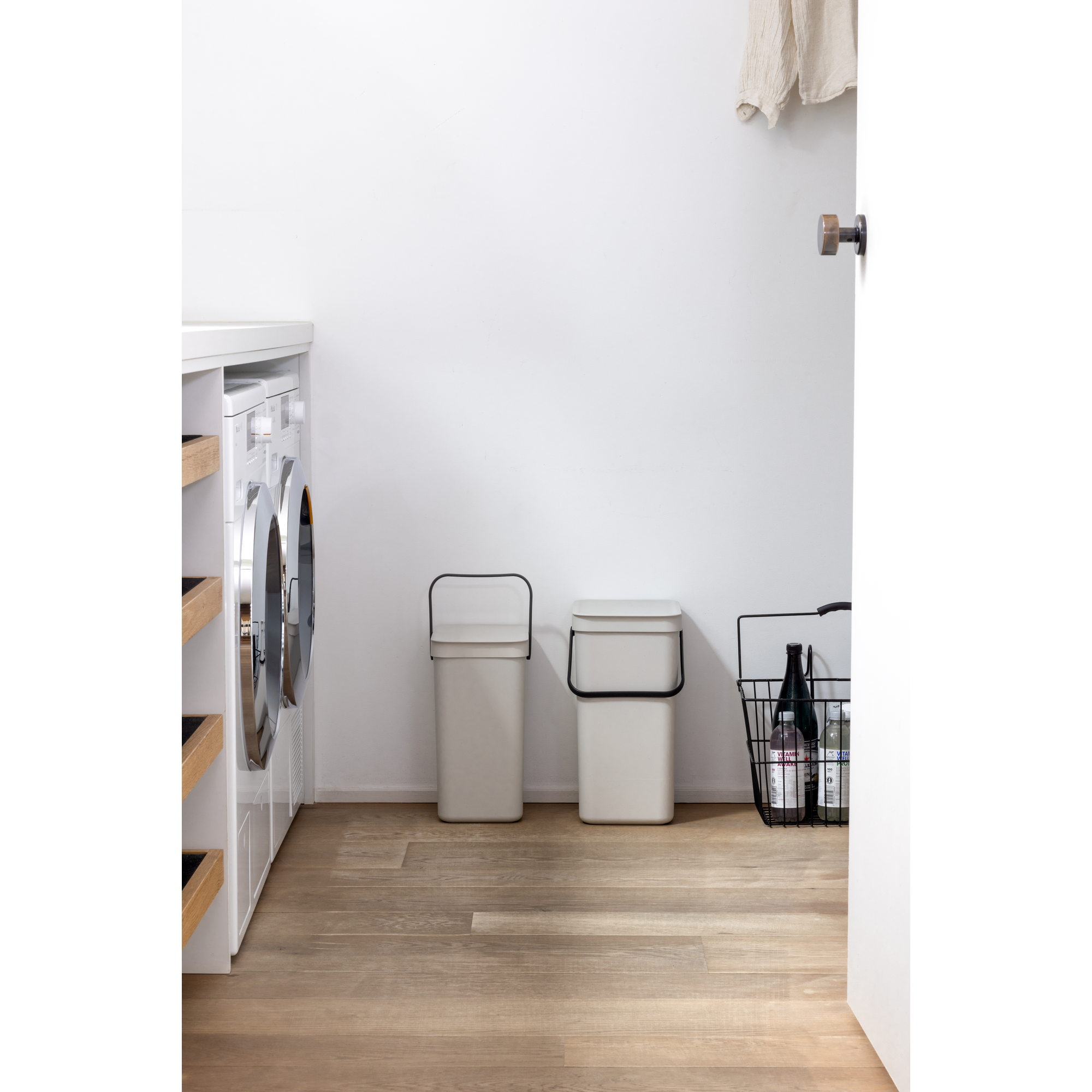 Wasruimte met wasmachine, twee prullenbakken en een mand met flessen.