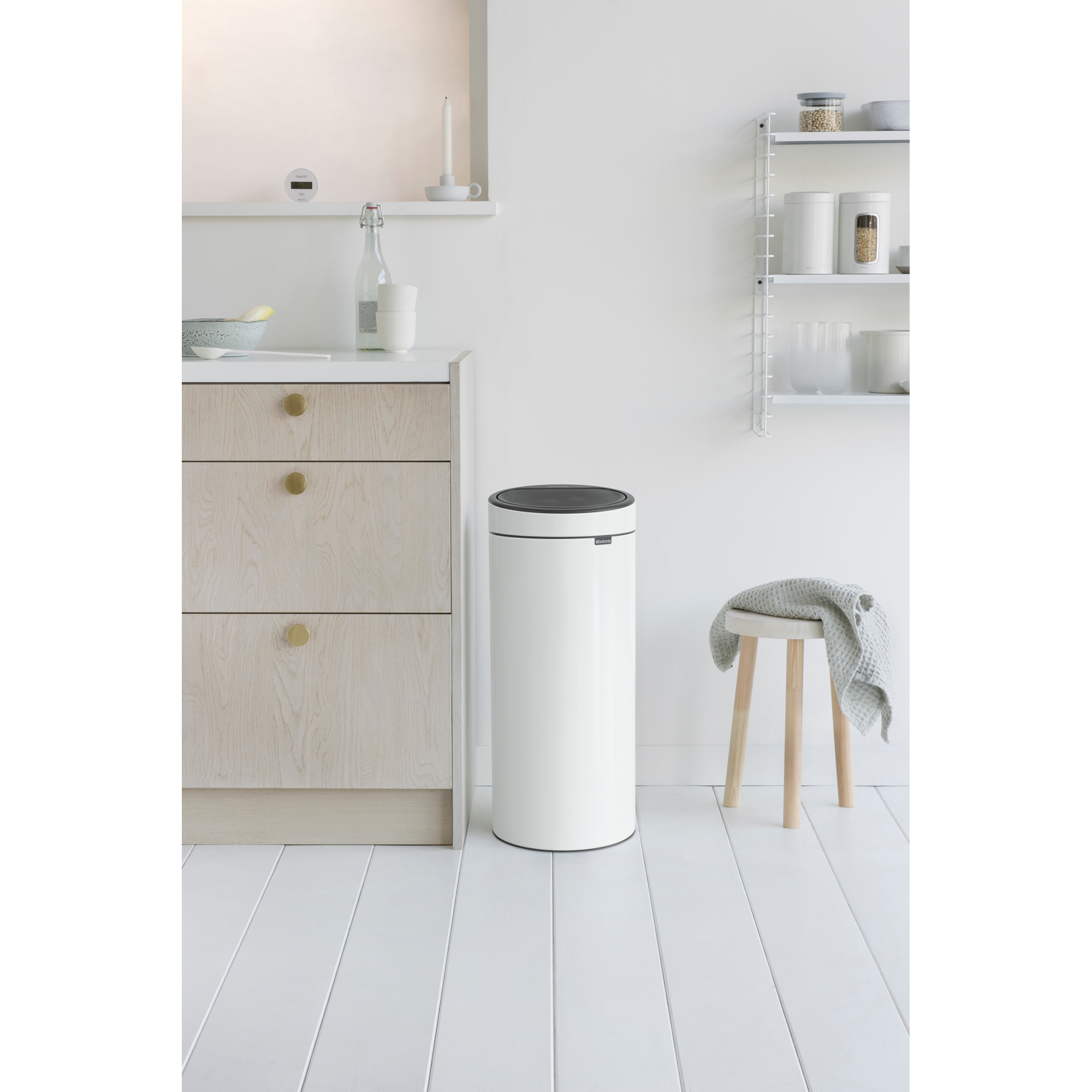 Een witte prullenbak naast een houten kast en een kruk met handdoek.