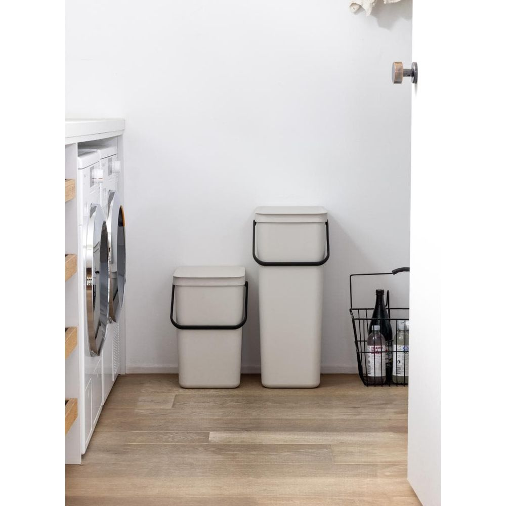 Twee beige prullenbakken en een wasrek met wasmachine op een houten vloer.