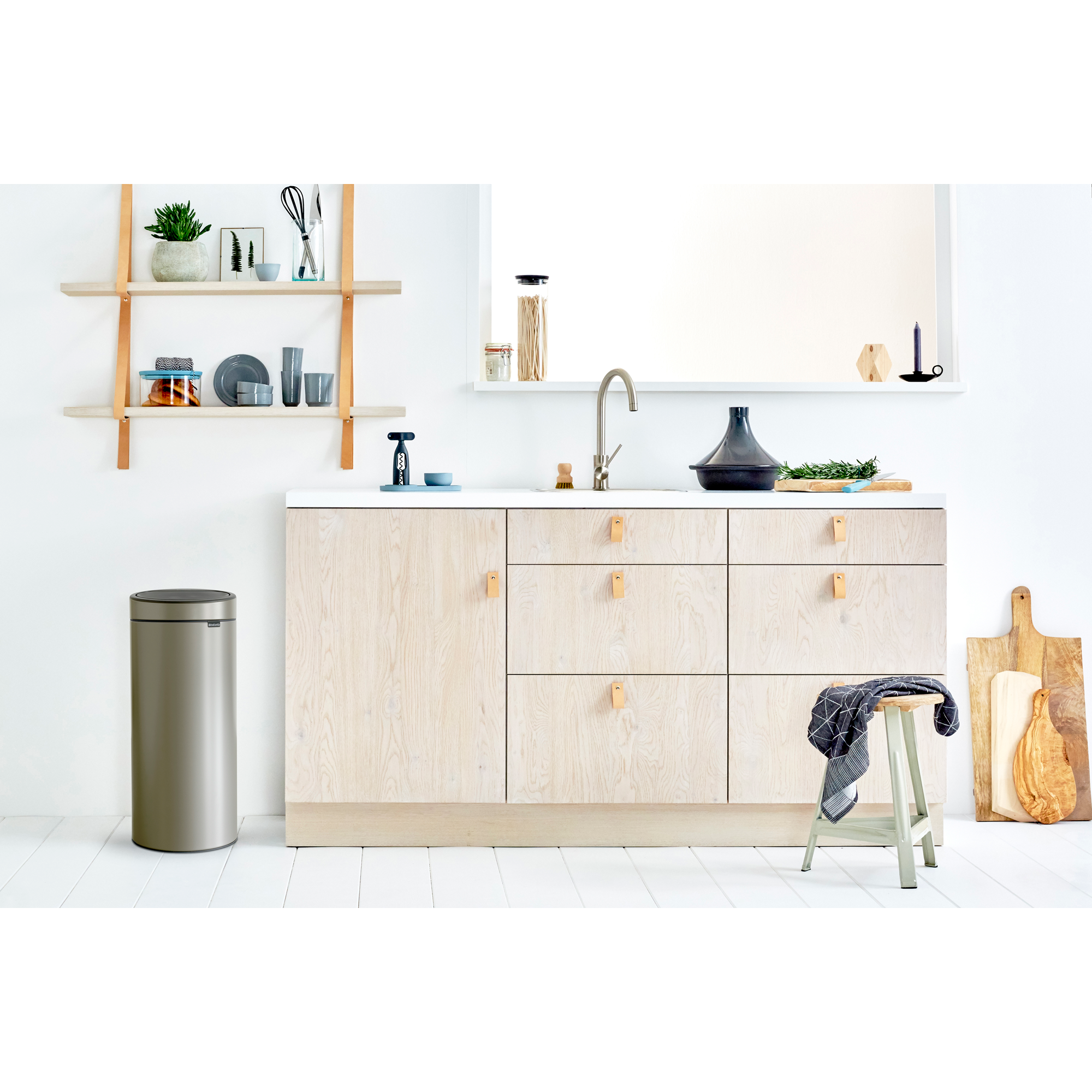 Een moderne keuken met houten kasten, een prullenbak en servies op planken.
