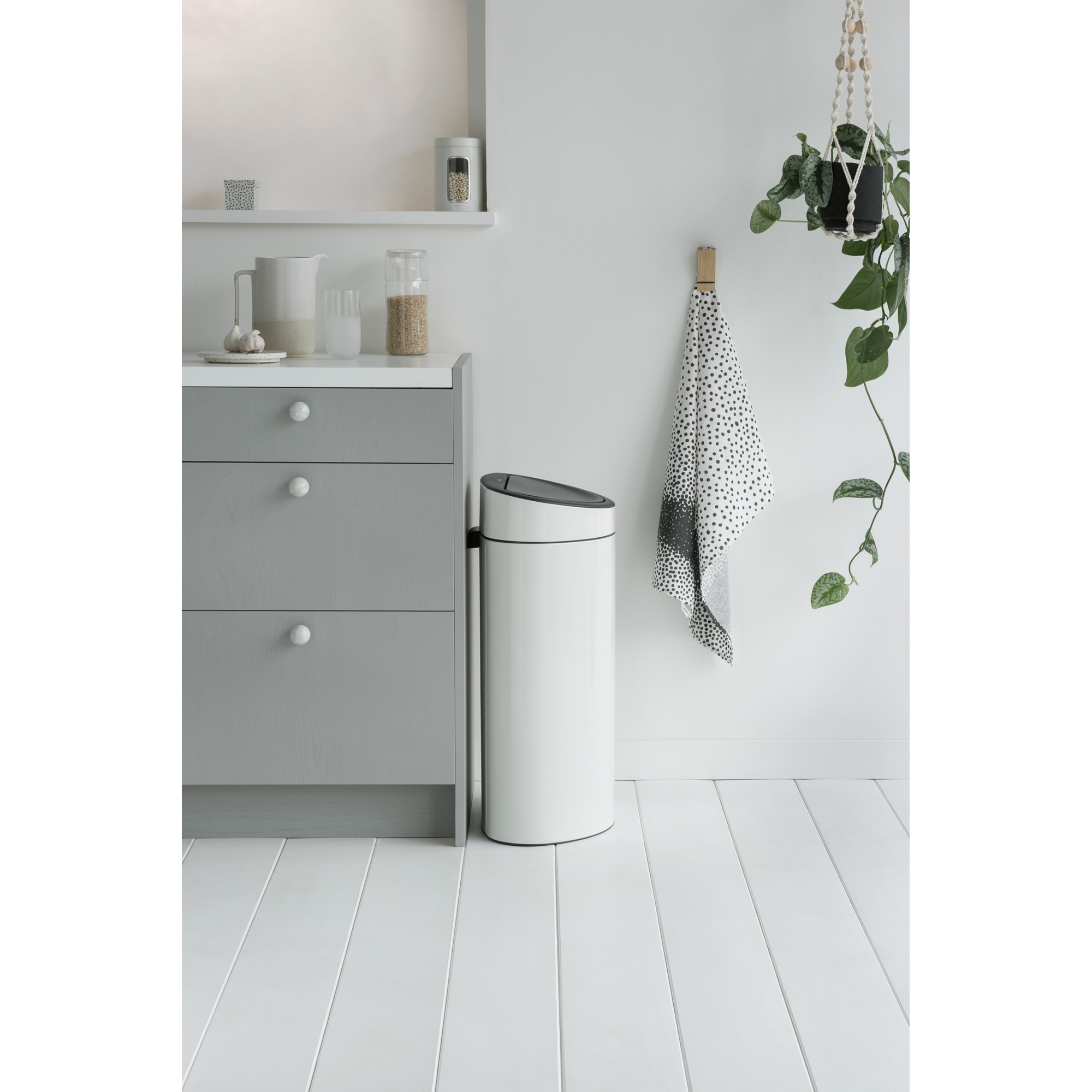 Een witte prullenbak naast een grijze kast met witte knoppen.