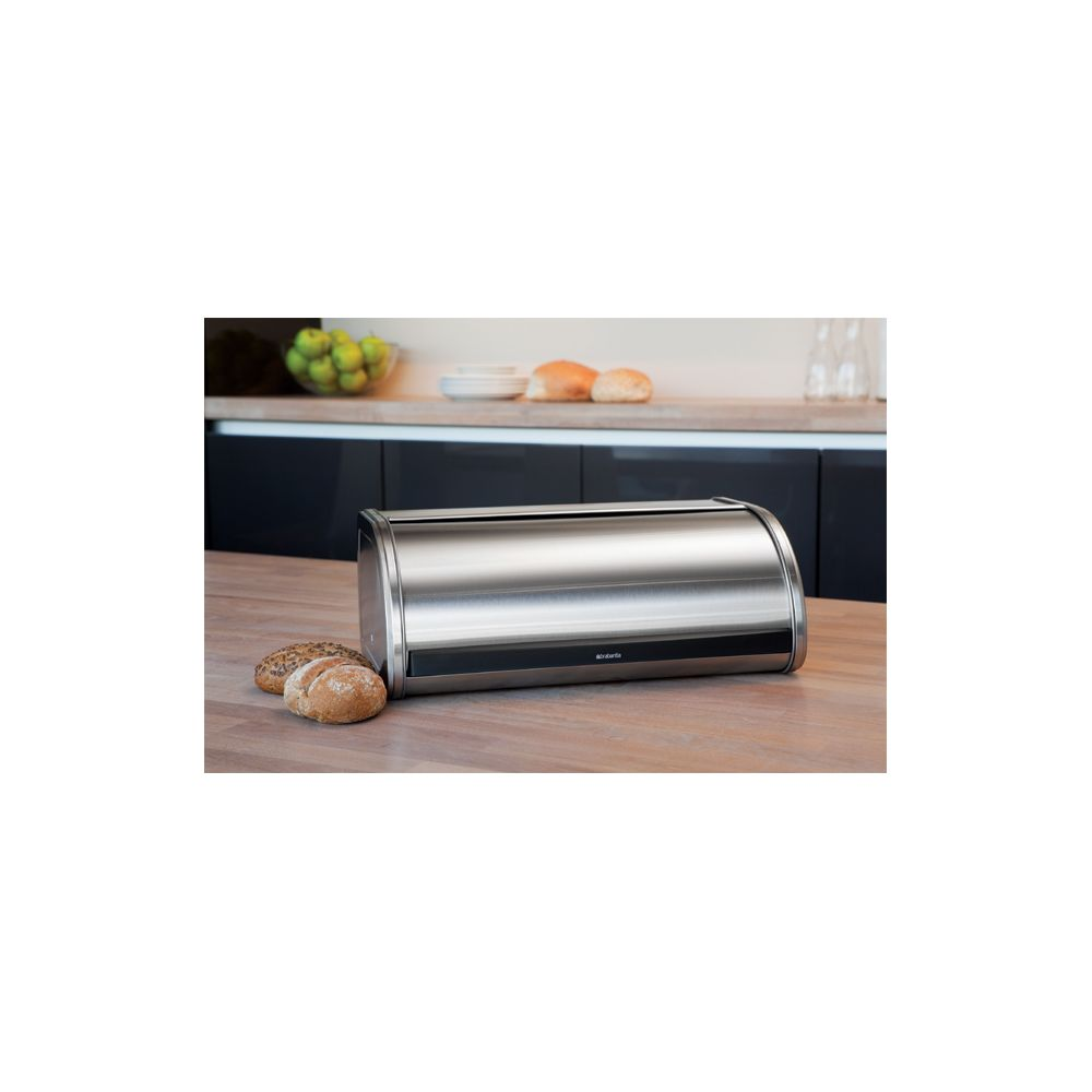 Een zilverkleurige broodtrommel met rolklep staat op een houten tafel voor broodjes.