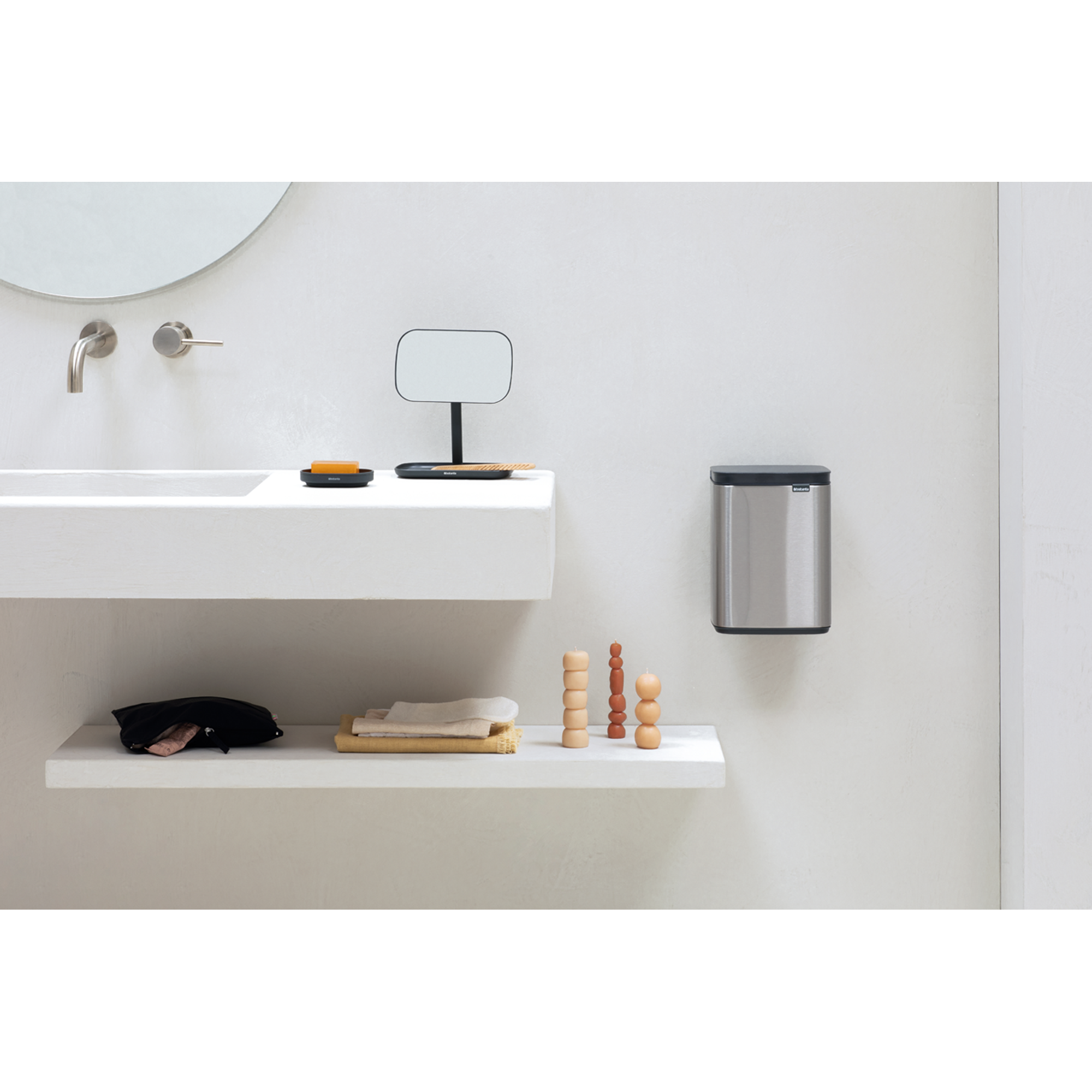 Een badkamer met een wastafel, spiegel, zeepbakje, prullenbak en decoratieve kaarsen.