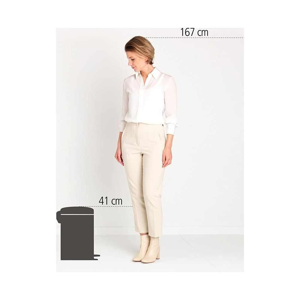 Een vrouw in een witte blouse en beige broek staat naast een prullenbak.