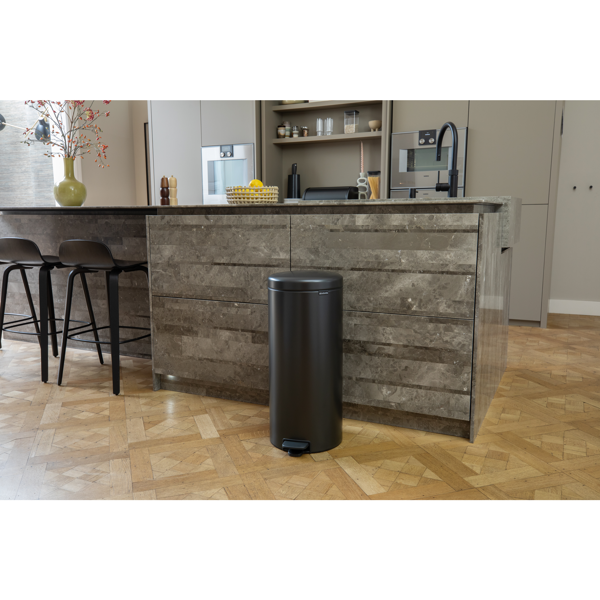 Un cubo de pedal negro está sobre un suelo de madera frente a una isla de cocina.