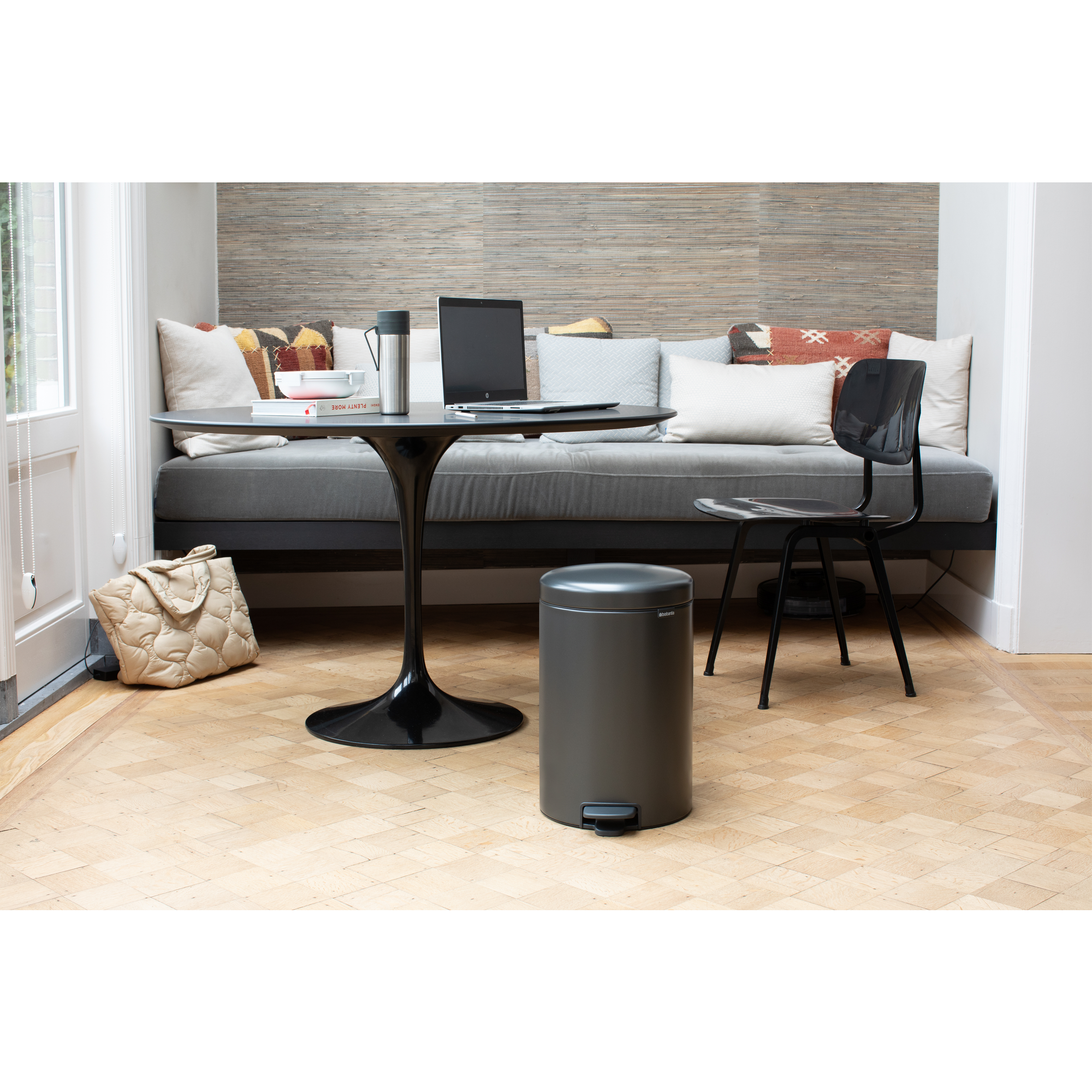Una habitación moderna con sofá, mesa, portátil, cubo de basura y silla.