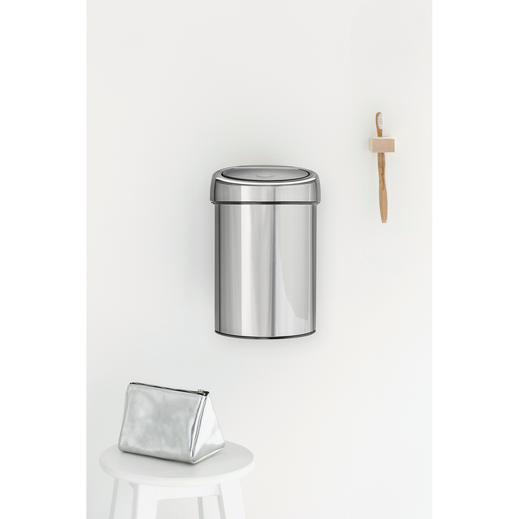 Een zilveren prullenbak en make-uptas staan op een kruk. Een tandenborstel is aan de muur bevestigd.