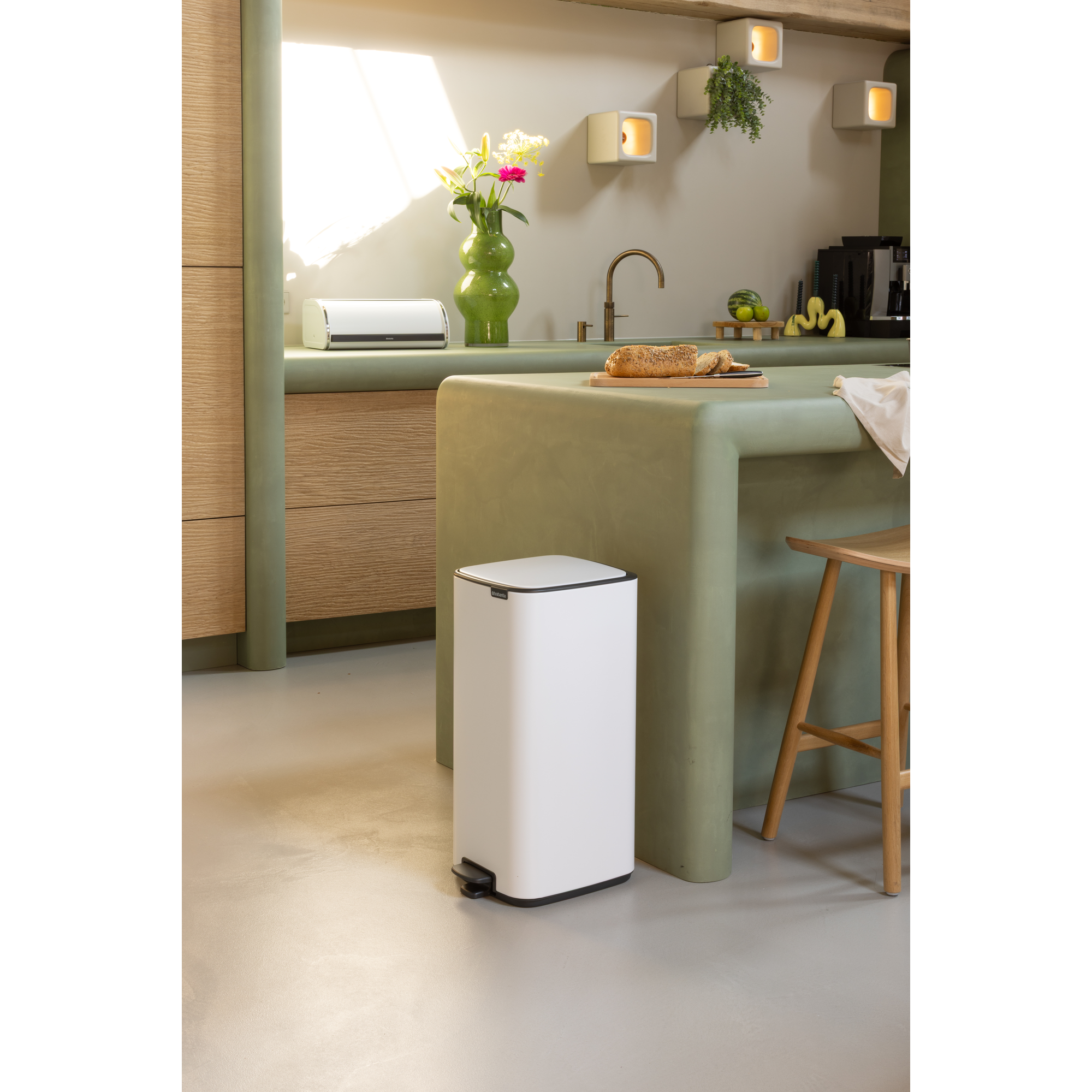 Moderne keuken met witte prullenbak, groen aanrecht, houten meubels en bloemen.