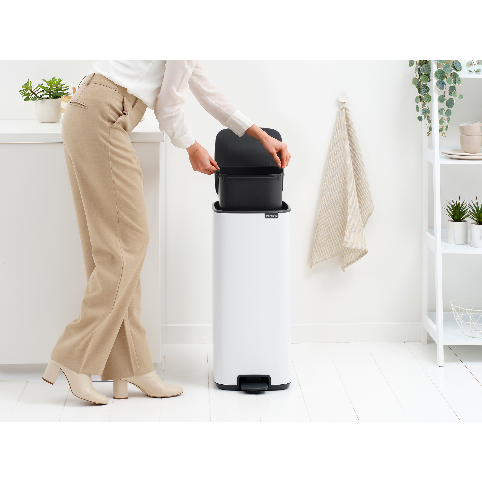 Een vrouw in beige broek en witte schoenen plaatst een vuilnisbak.