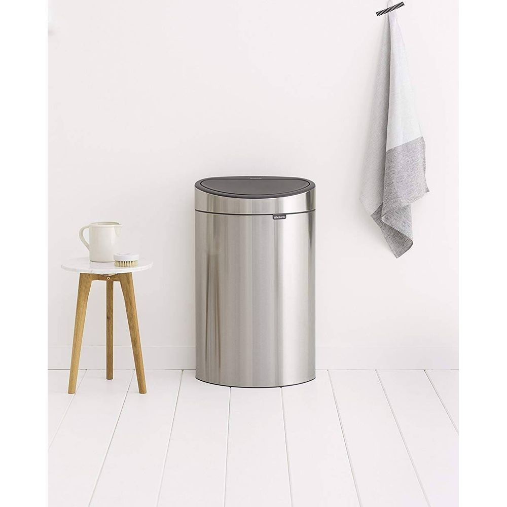 Een zilveren prullenbak met zwart deksel staat op een witte houten vloer.