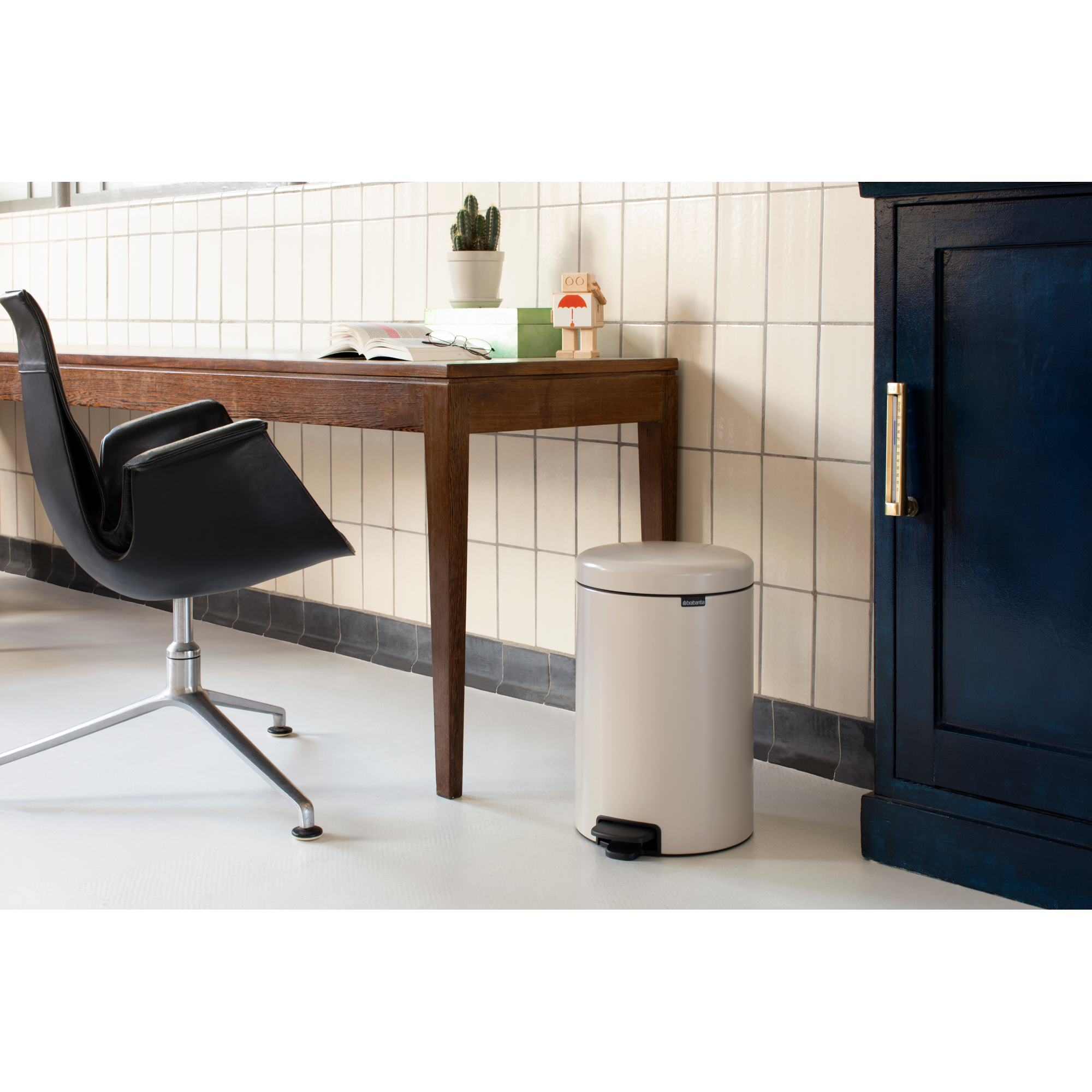 Een beige pedaalemmer naast een houten bureau en een zwarte stoel.