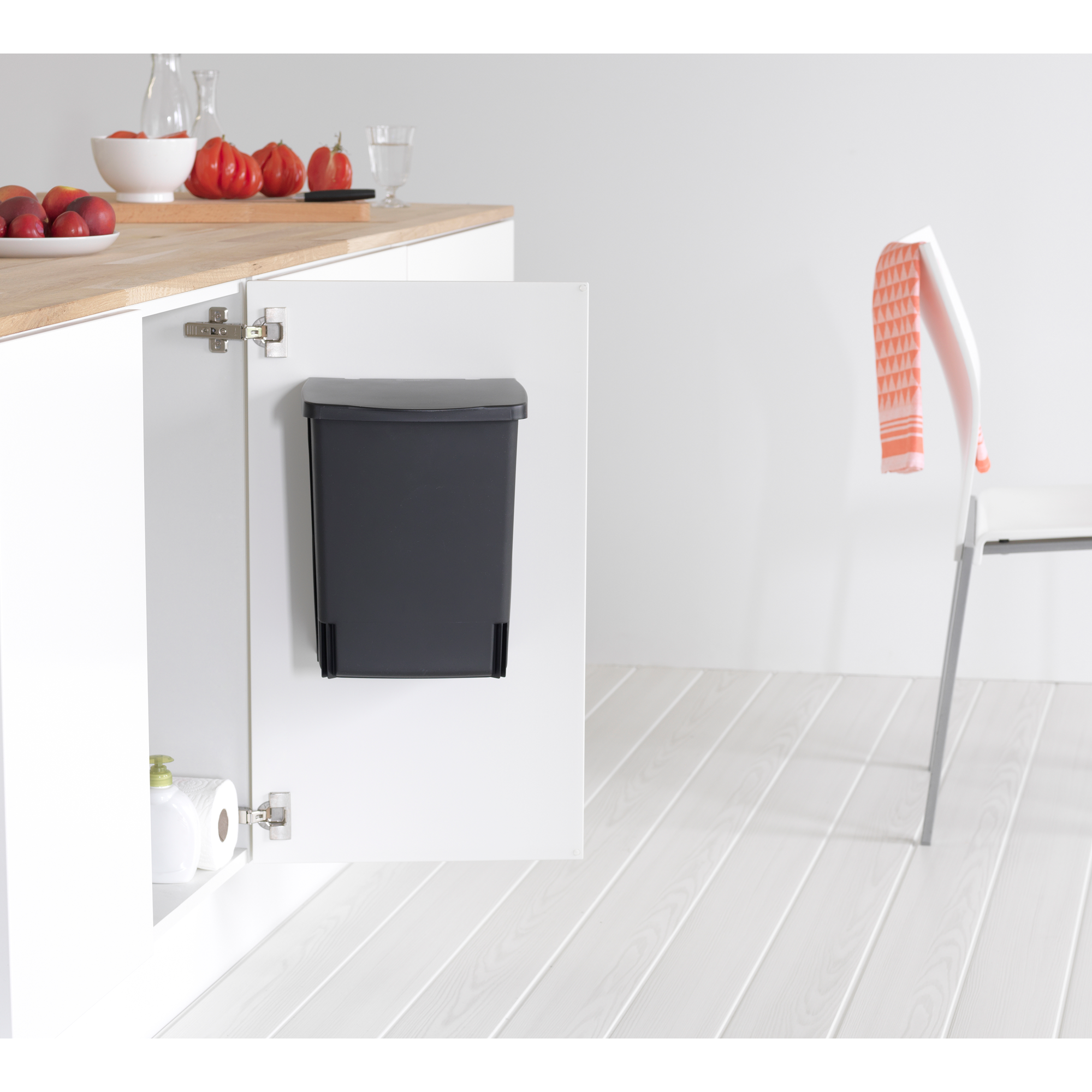 Donkergrijze prullenbak in een open keukenkastje naast toiletpapier.