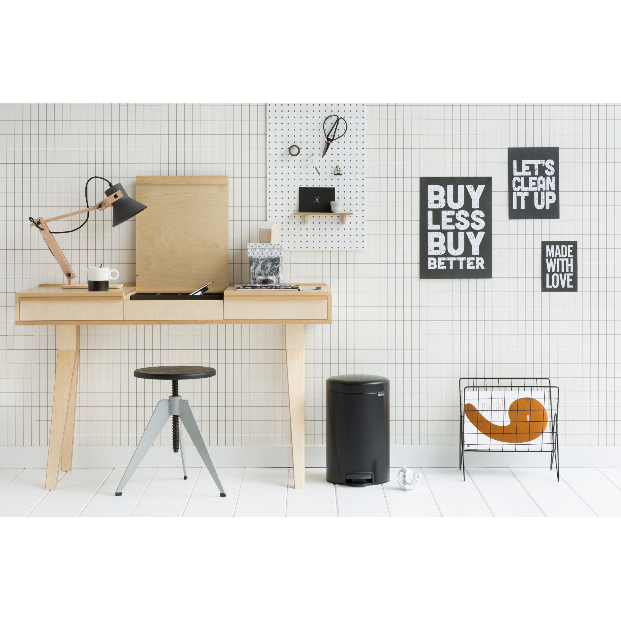 Een bureau met lamp, kruk, prullenbak en wanddecoratie.