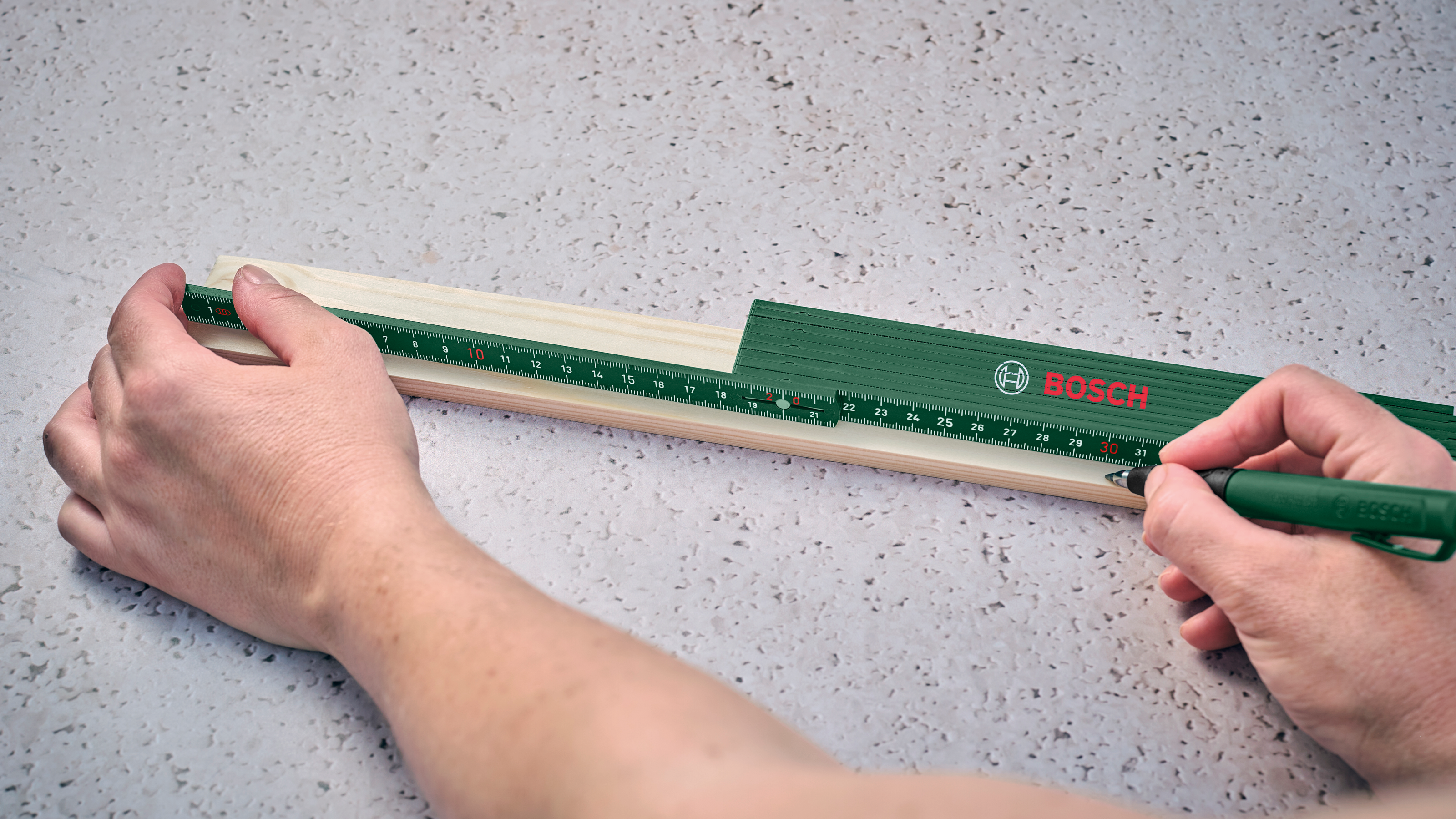 Eine Person misst Holz mit einem grünen Klappmaßstab von Bosch.