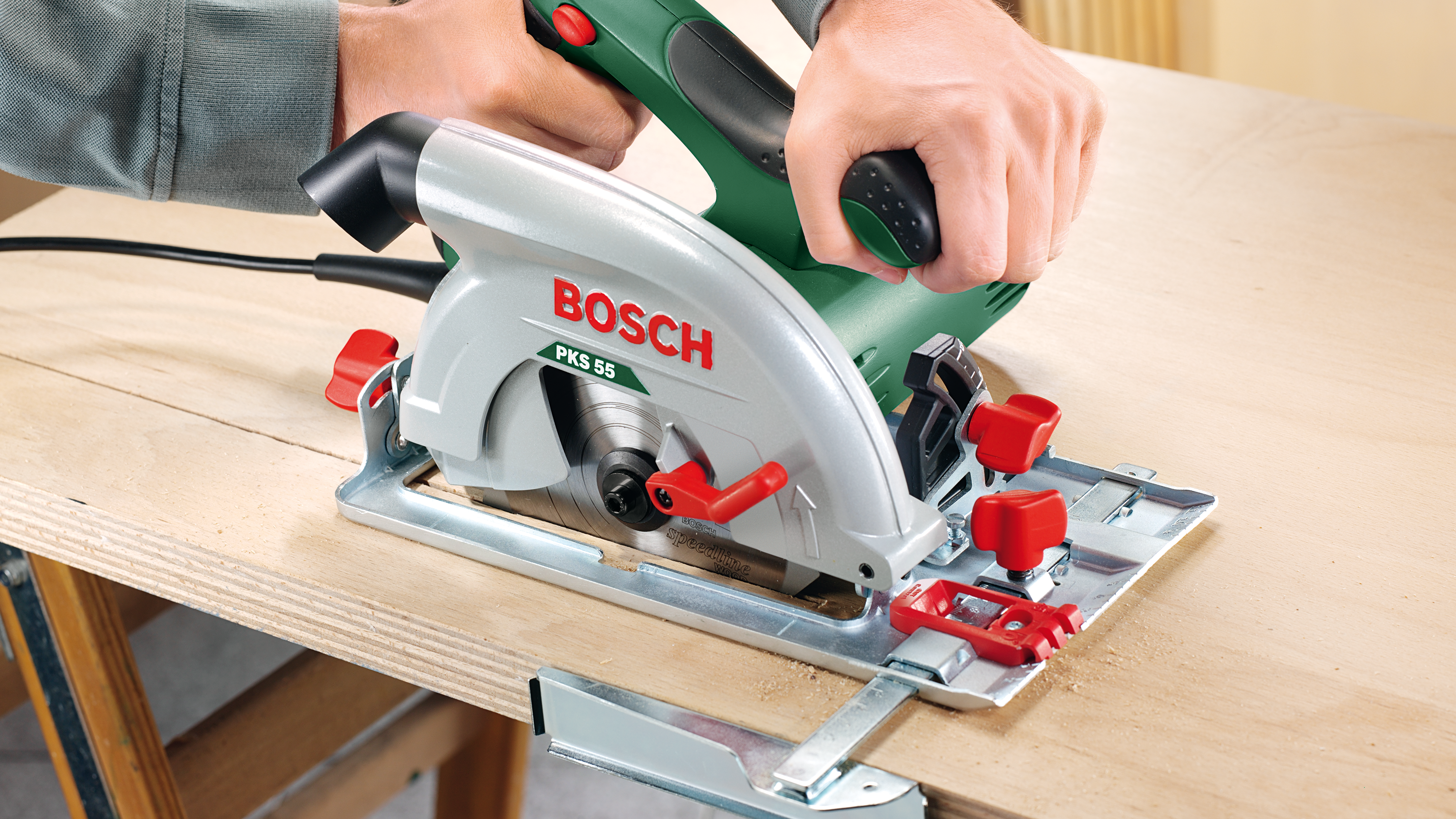 A hand holds a green Bosch circular saw cutting wood.