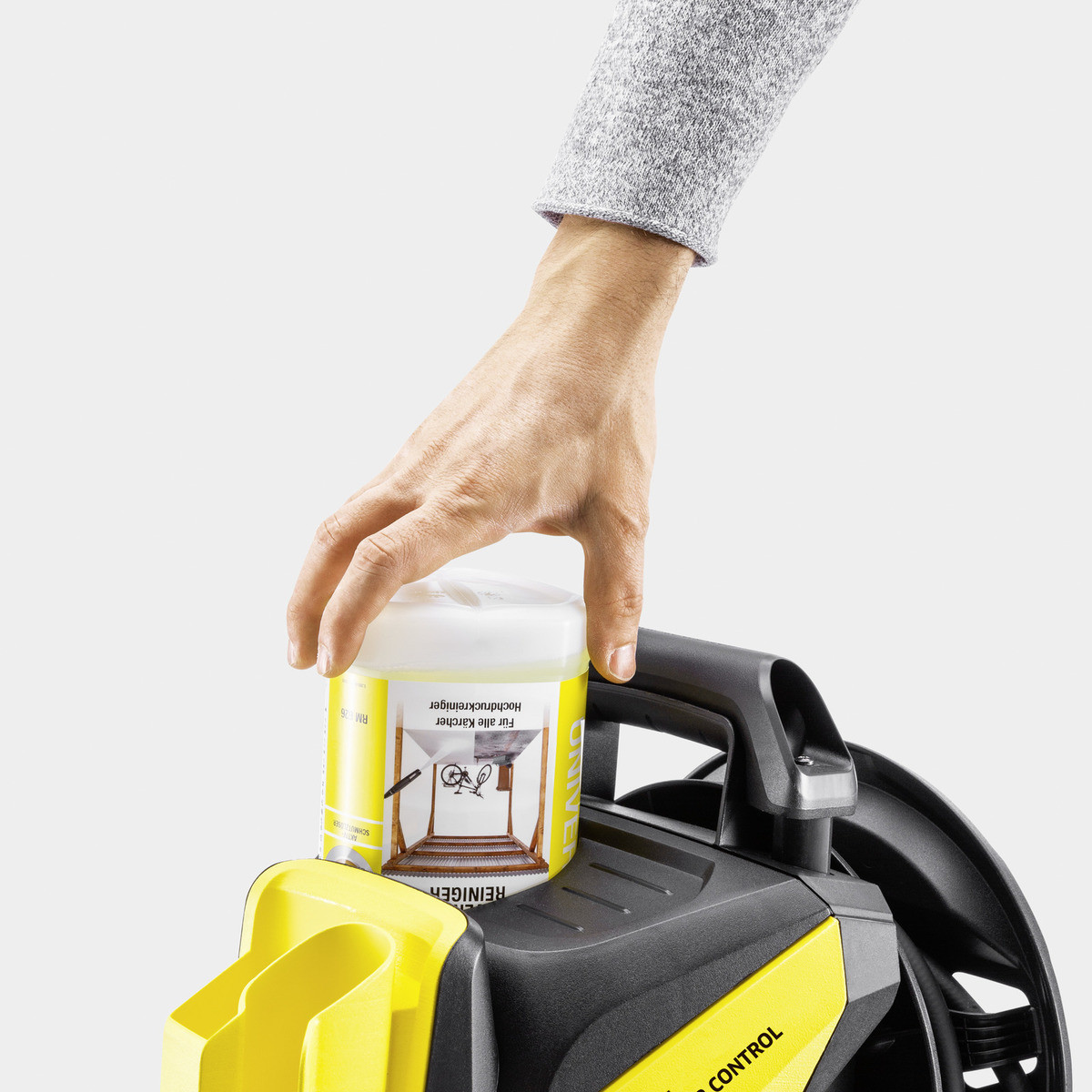 Mano sujetando botella de líquido de limpieza amarillo sobre hidrolimpiadora amarilla y negra.