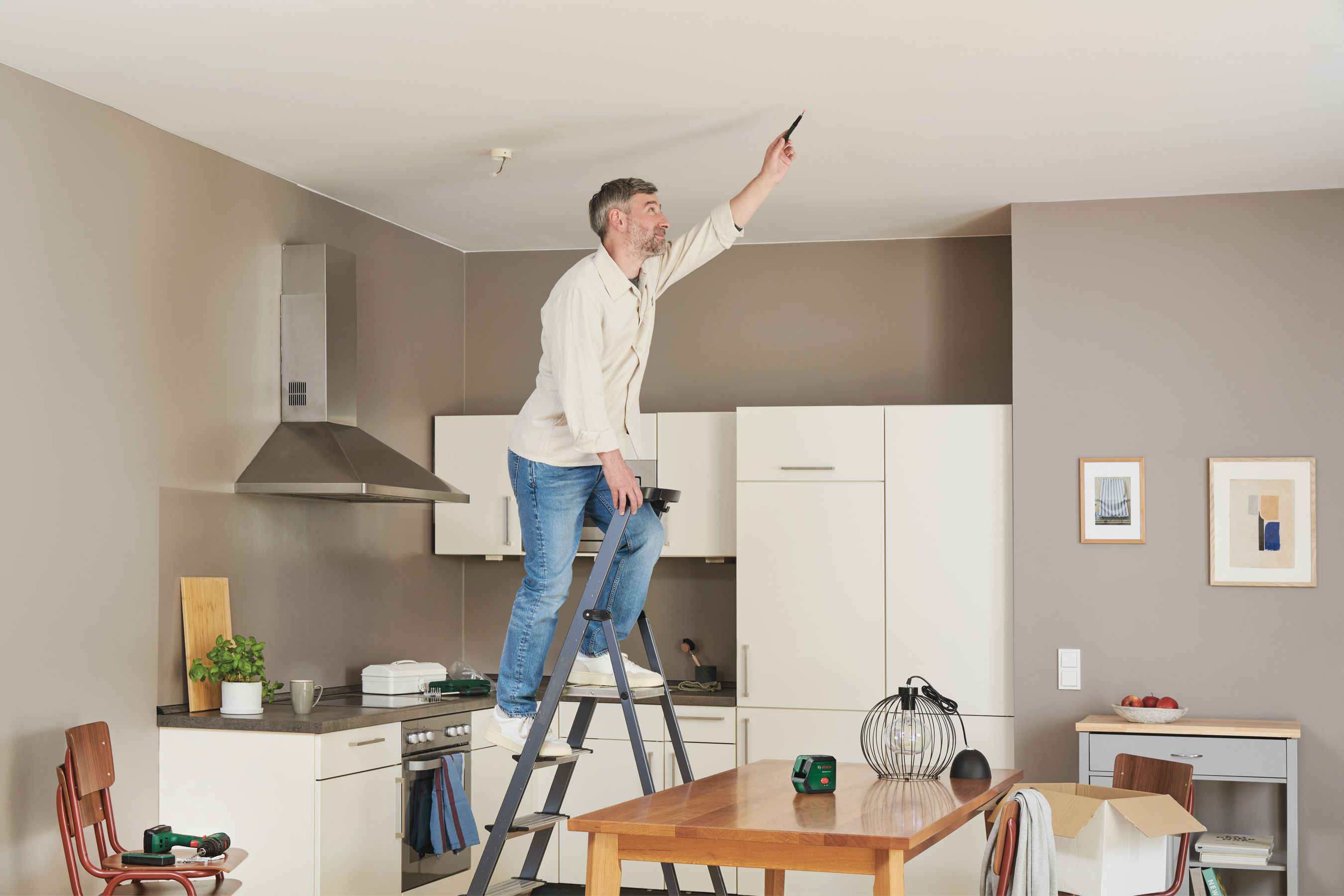Un uomo su una scala controlla il soffitto, con cucina e tavolo da pranzo vicini.